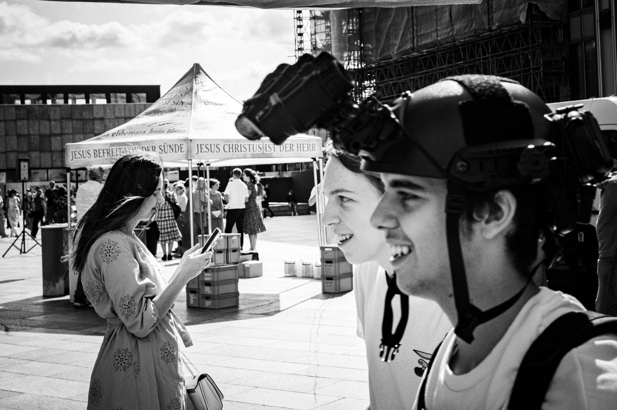 Black and white city scene with people outdoors, two smiling friends in focus and a woman using her phone.