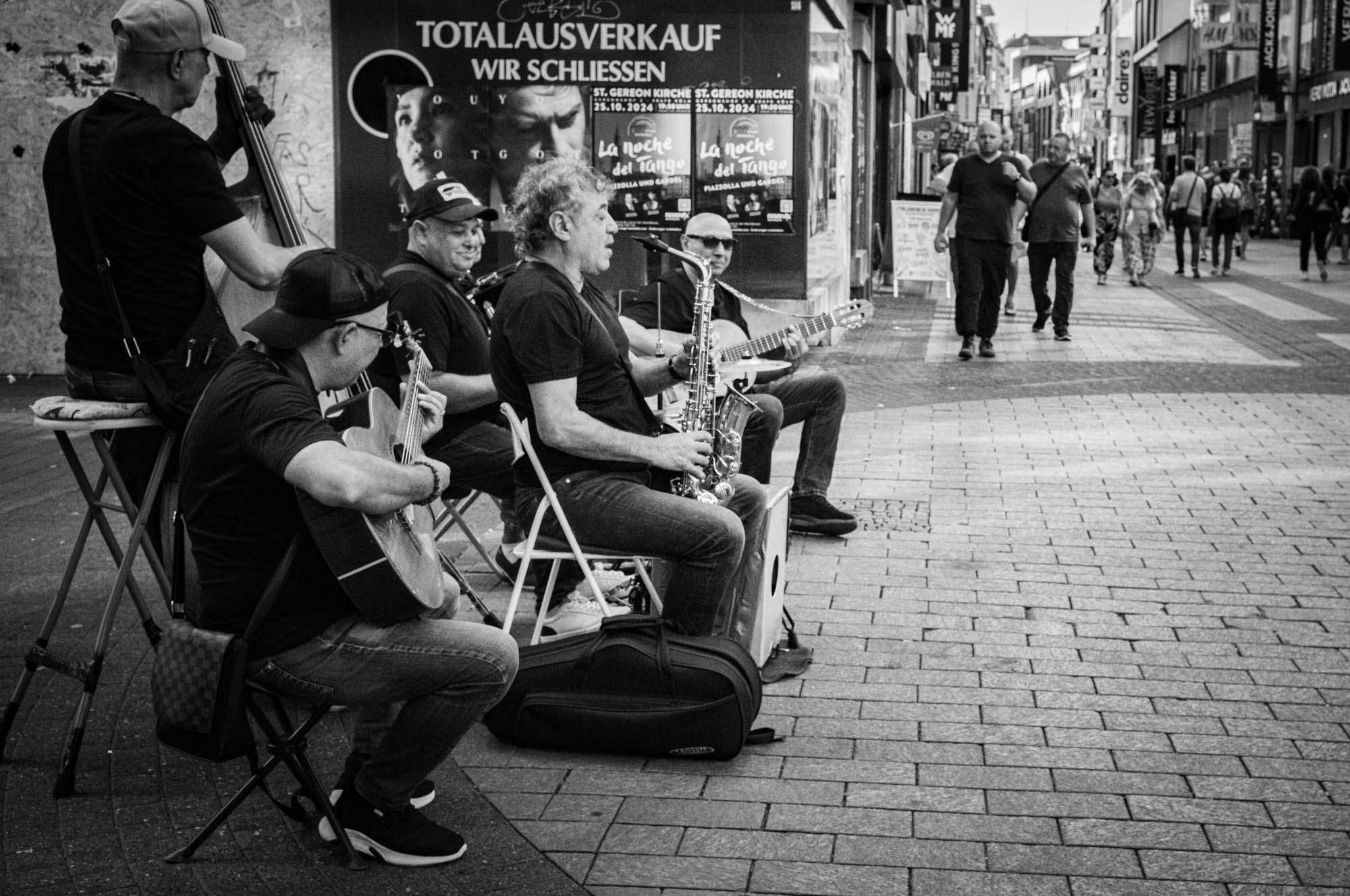 Street musicians performing in a lively city area, with pedestrians walking by, black and white photo.