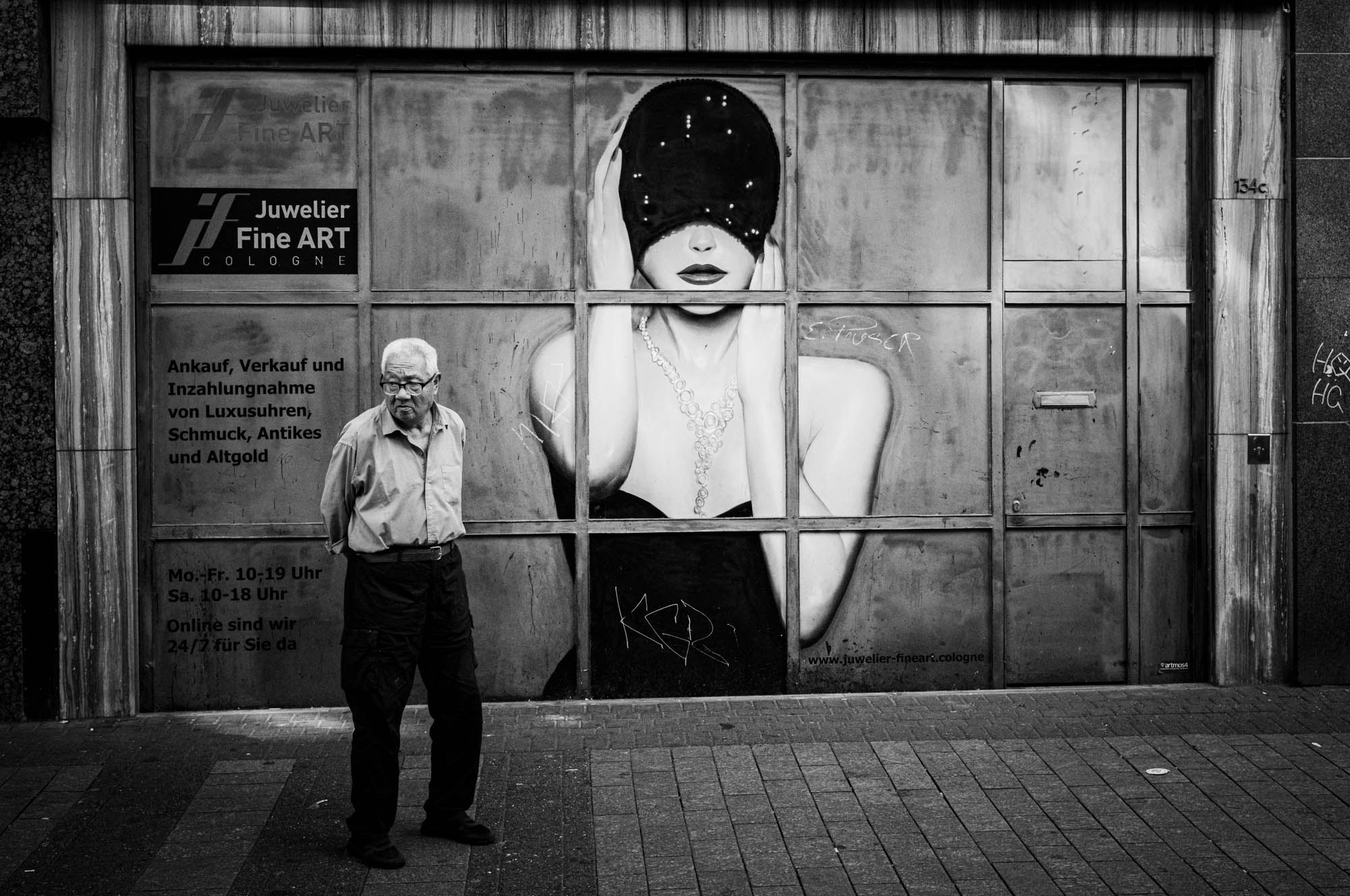 Man standing in front of jewelry store with mural artwork in Cologne, black and white photo.