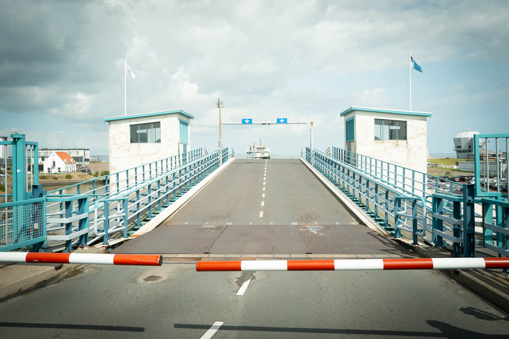 Raised drawbridge with red barrier, awaiting ferry arrival under cloudy sky.