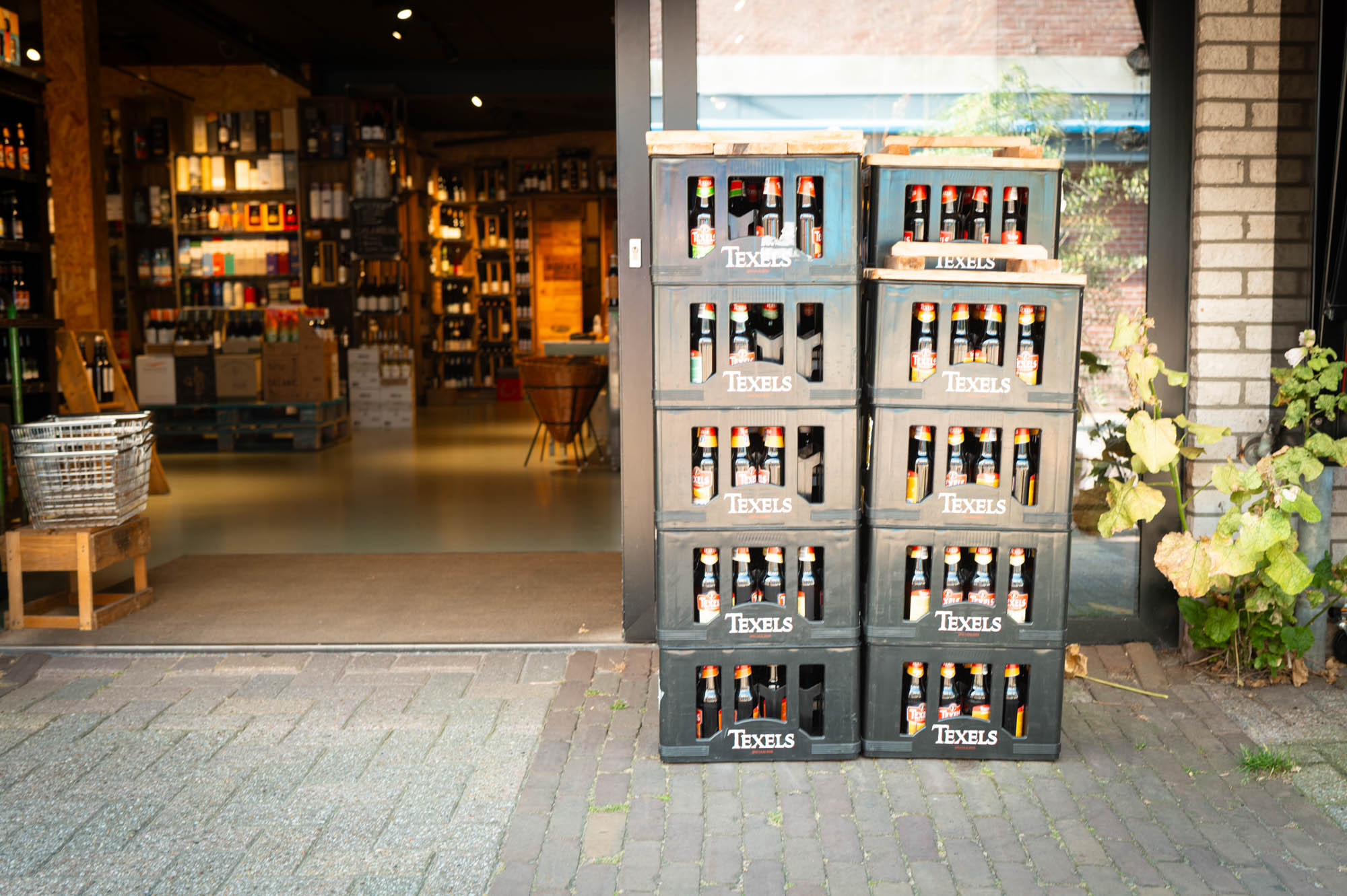 Stacked Texels beer crates outside a well-stocked liquor store entrance.