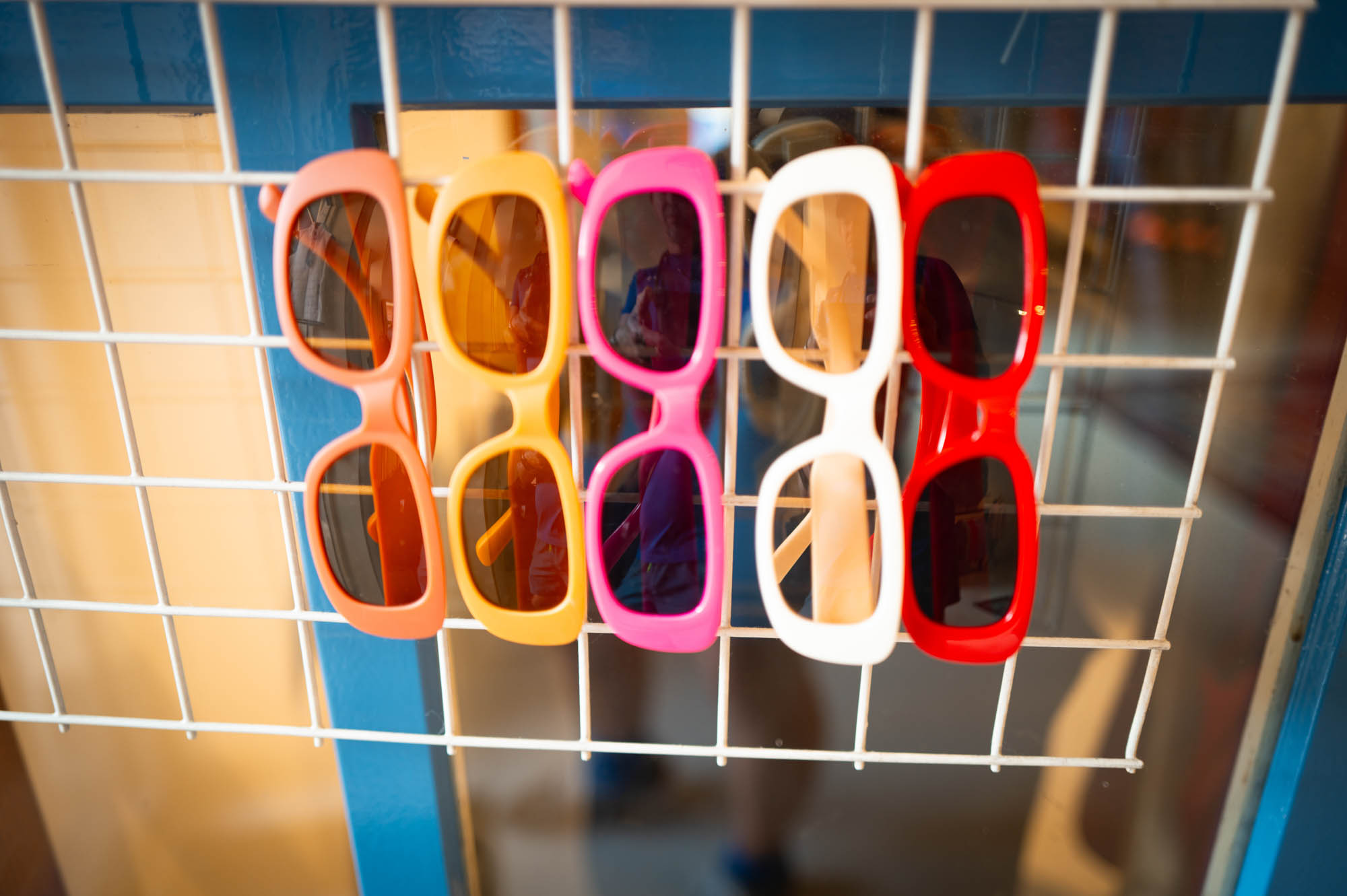 Colorful sunglasses displayed on a metal rack in a shop window.