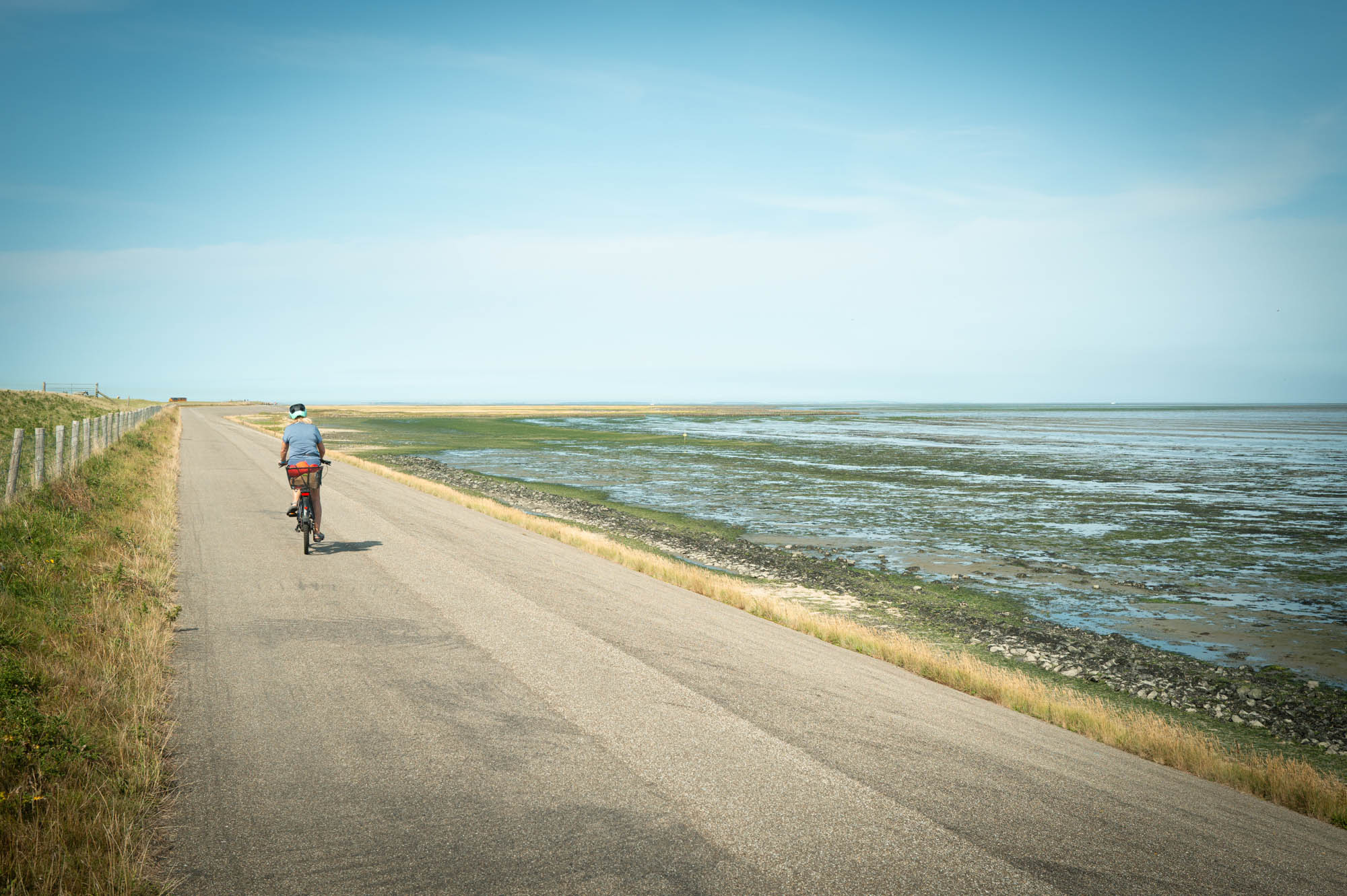 Person cycling on a coastal road next to the sea under a clear blue sky.