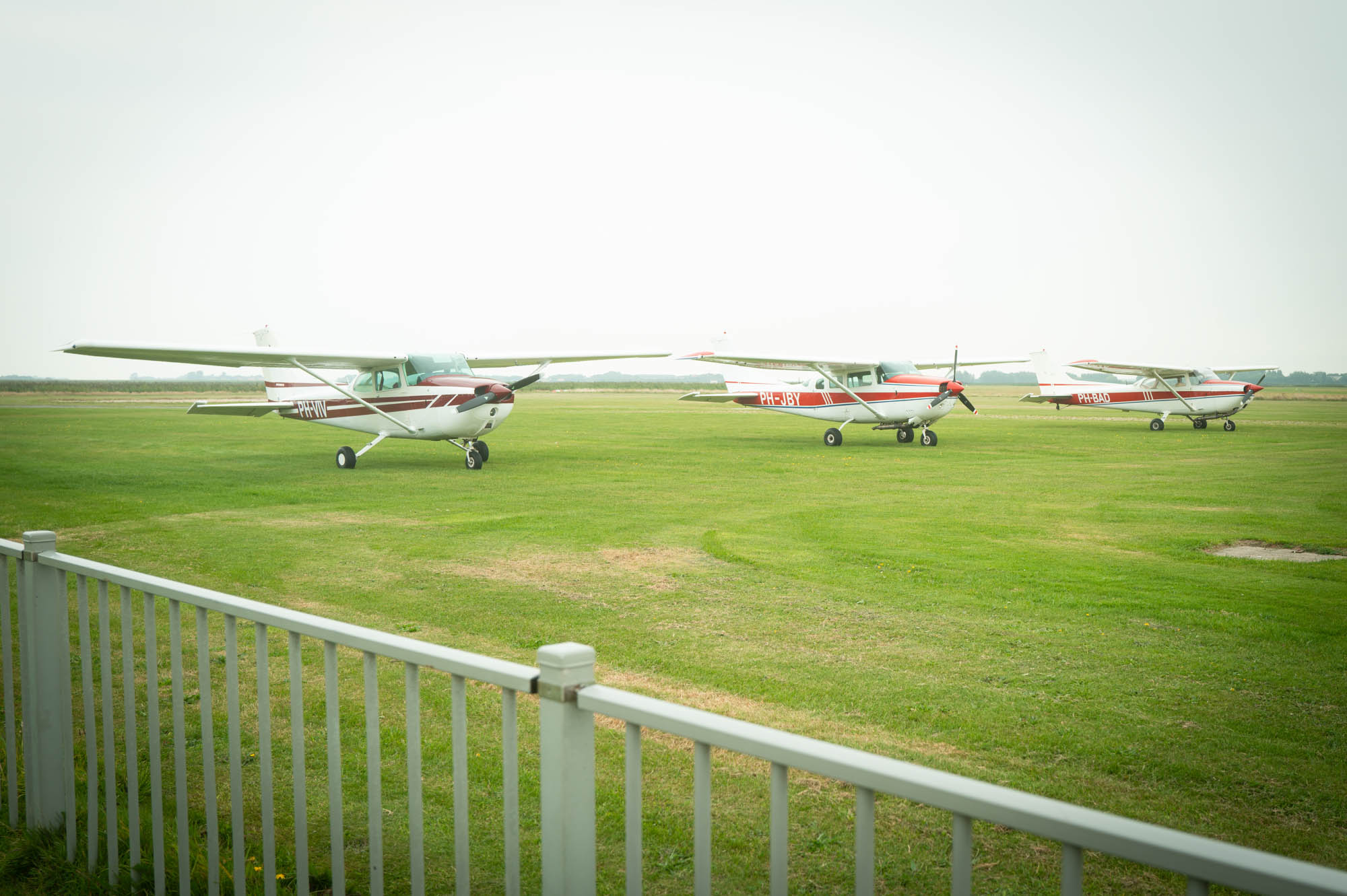 Small airplanes parked on a grassy field next to a white fence, under a clear sky.