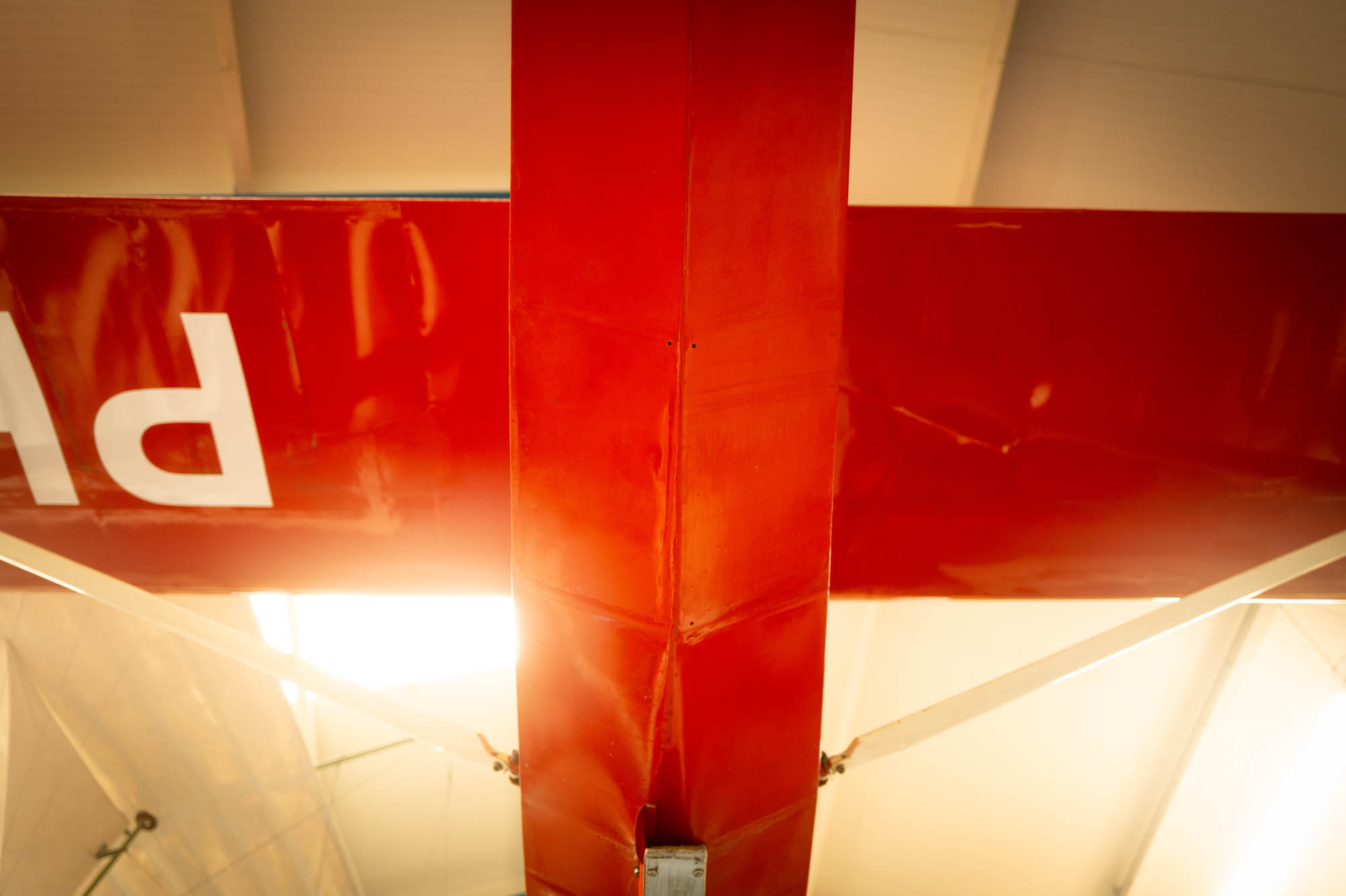 Close-up view of a red airplane tail inside a hangar, capturing a sunlit geometric perspective.