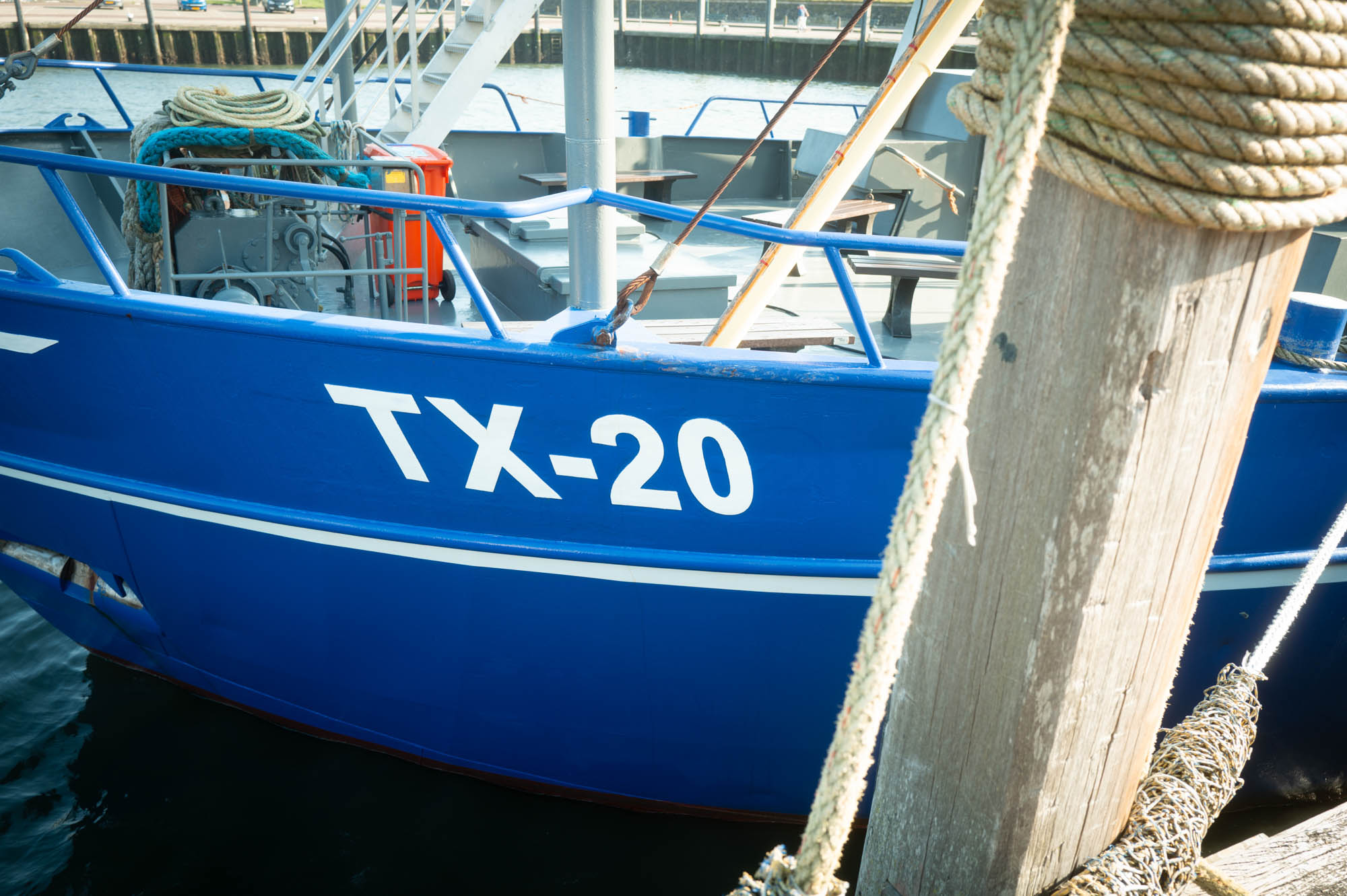 Blue boat labeled TX-20 moored at a dock with ropes.