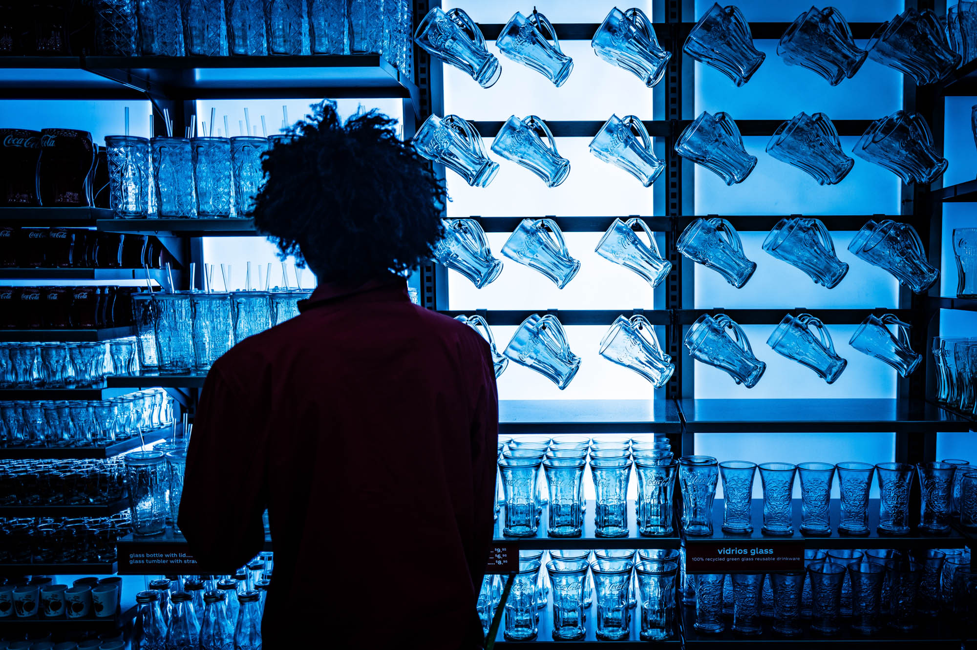 Person viewing glassware display with various cups and mugs on blue-lit shelves.