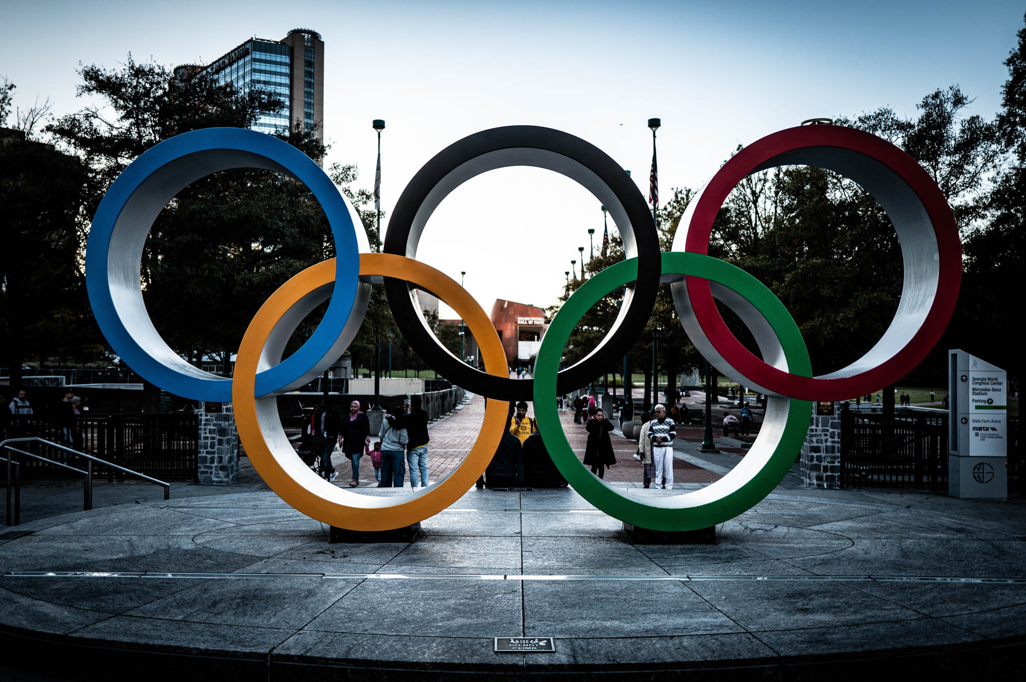 Olympic rings sculpture at Centennial Olympic Park, Atlanta, Georgia, with people and trees in the background.