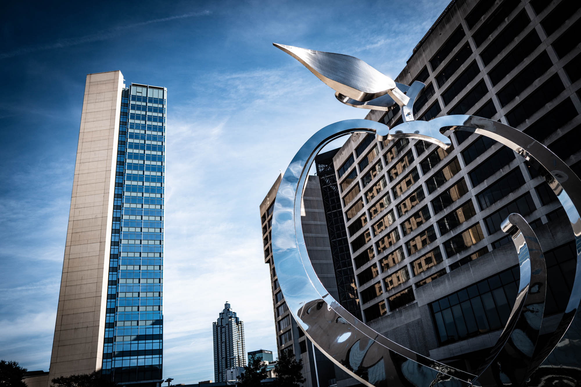 Modern skyscrapers and large metal sculpture against a clear blue sky in an urban landscape scene.