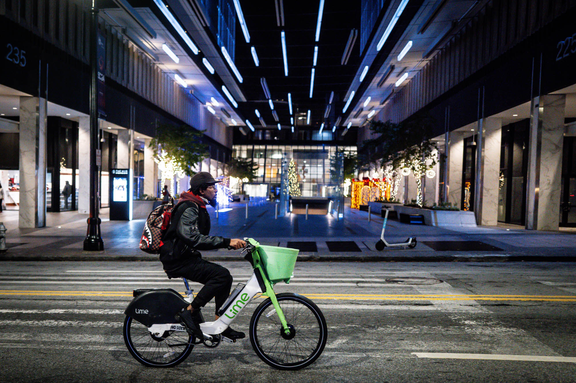 Person riding Lime bike at night through festive city street, adorned with holiday lights.