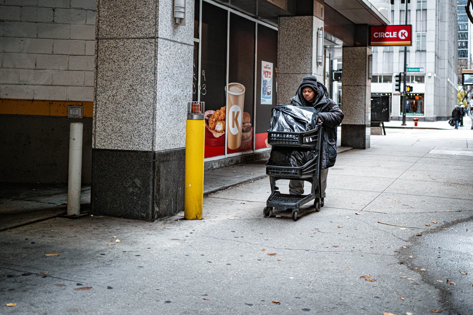Person pushing cart past Circle K store on urban street corner.