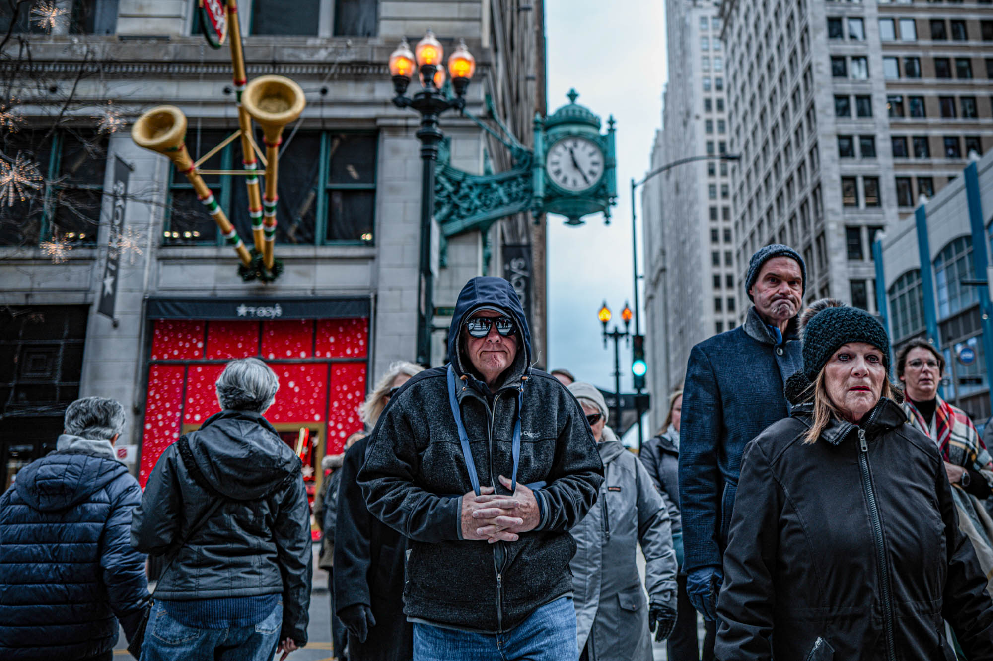 People walking in a busy city street near a historical building with a clock and holiday decorations overhead.
