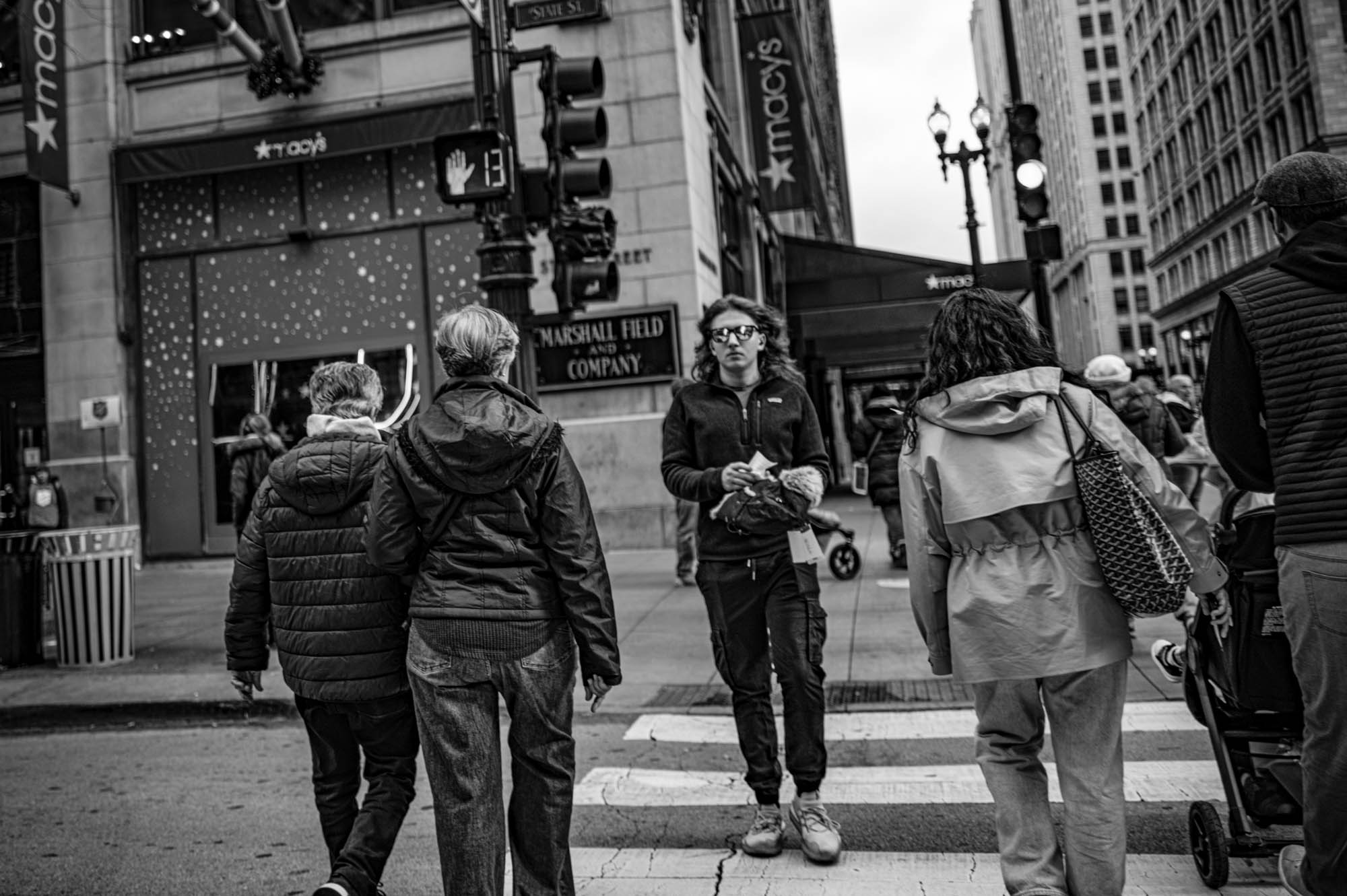 People crossing a busy street in front of Macy's store, urban city scene in black and white.