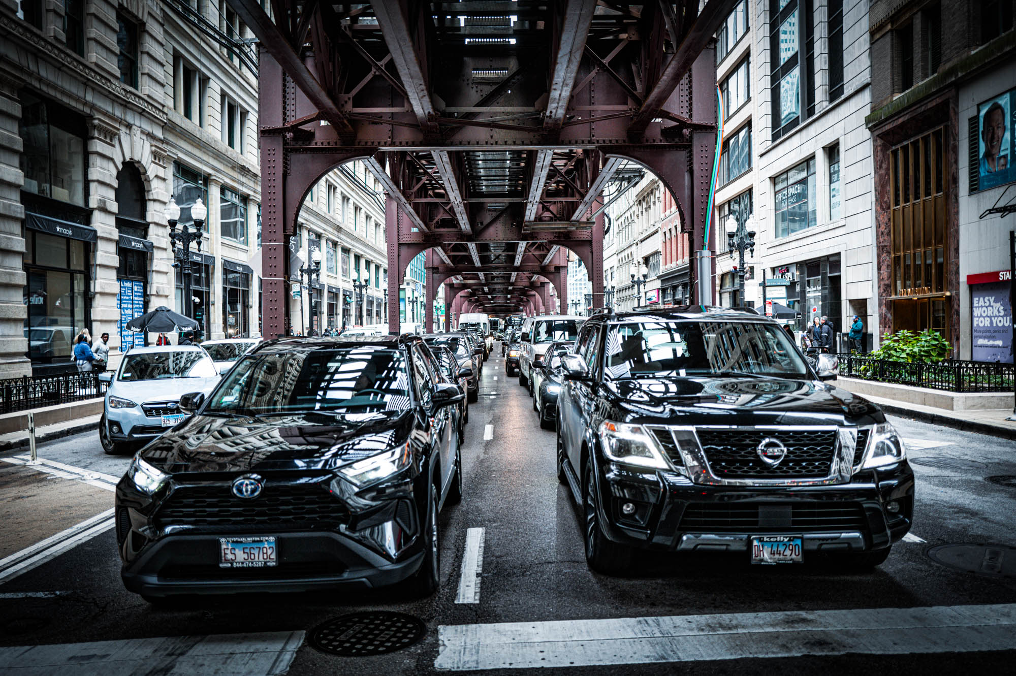 Traffic on urban street under railway tracks with buildings in background.