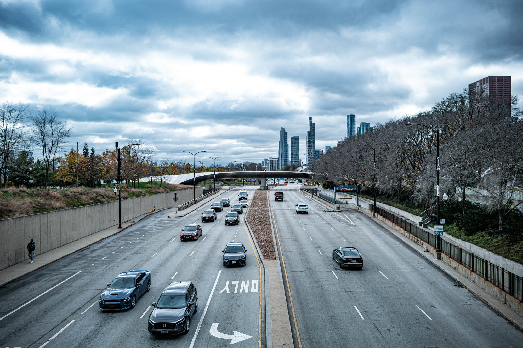 Cars on a busy highway with a cloudy sky and city skyline in the background.