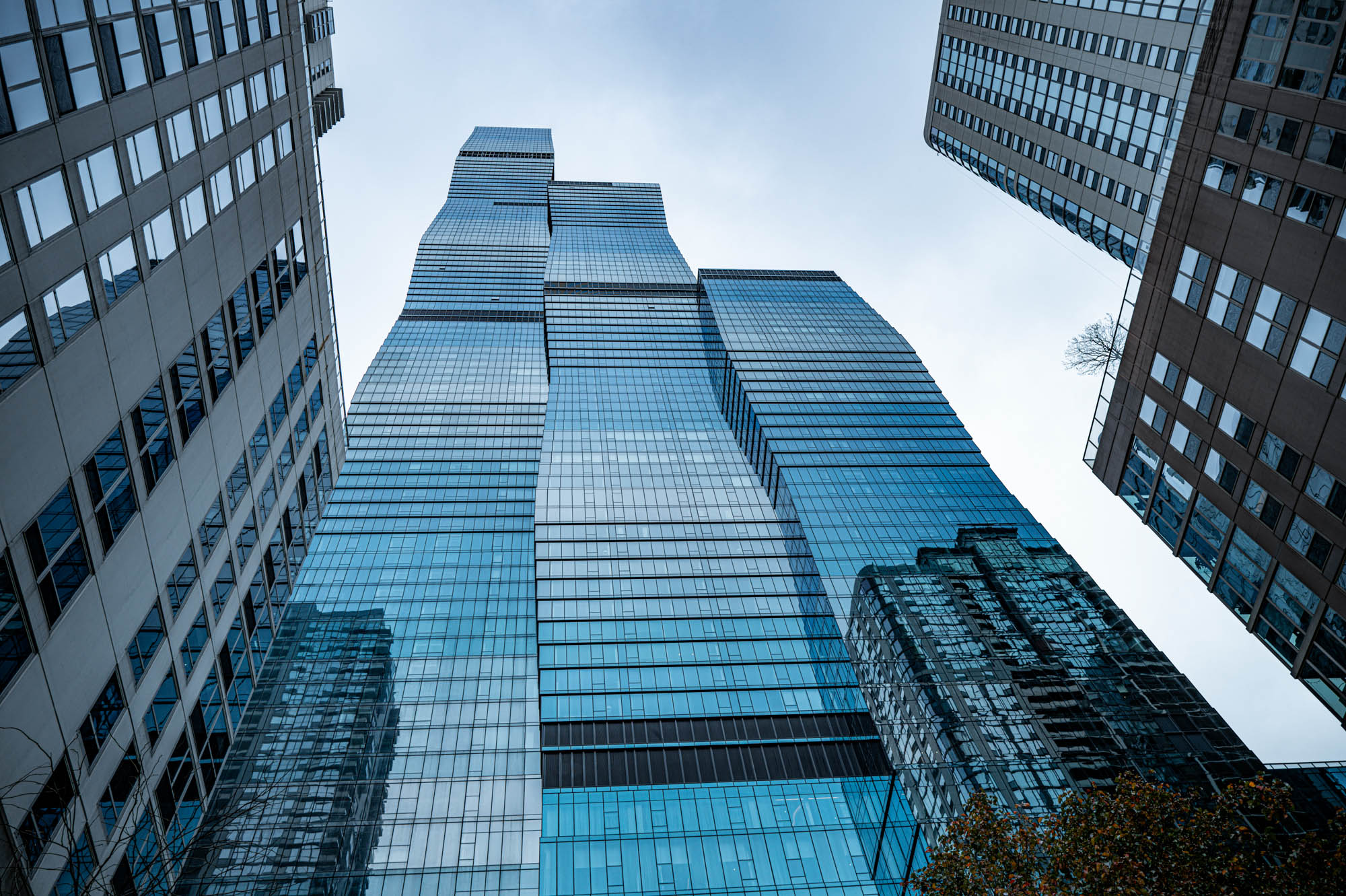 Futuristic glass skyscraper with blue reflections against the sky, framed by surrounding buildings.