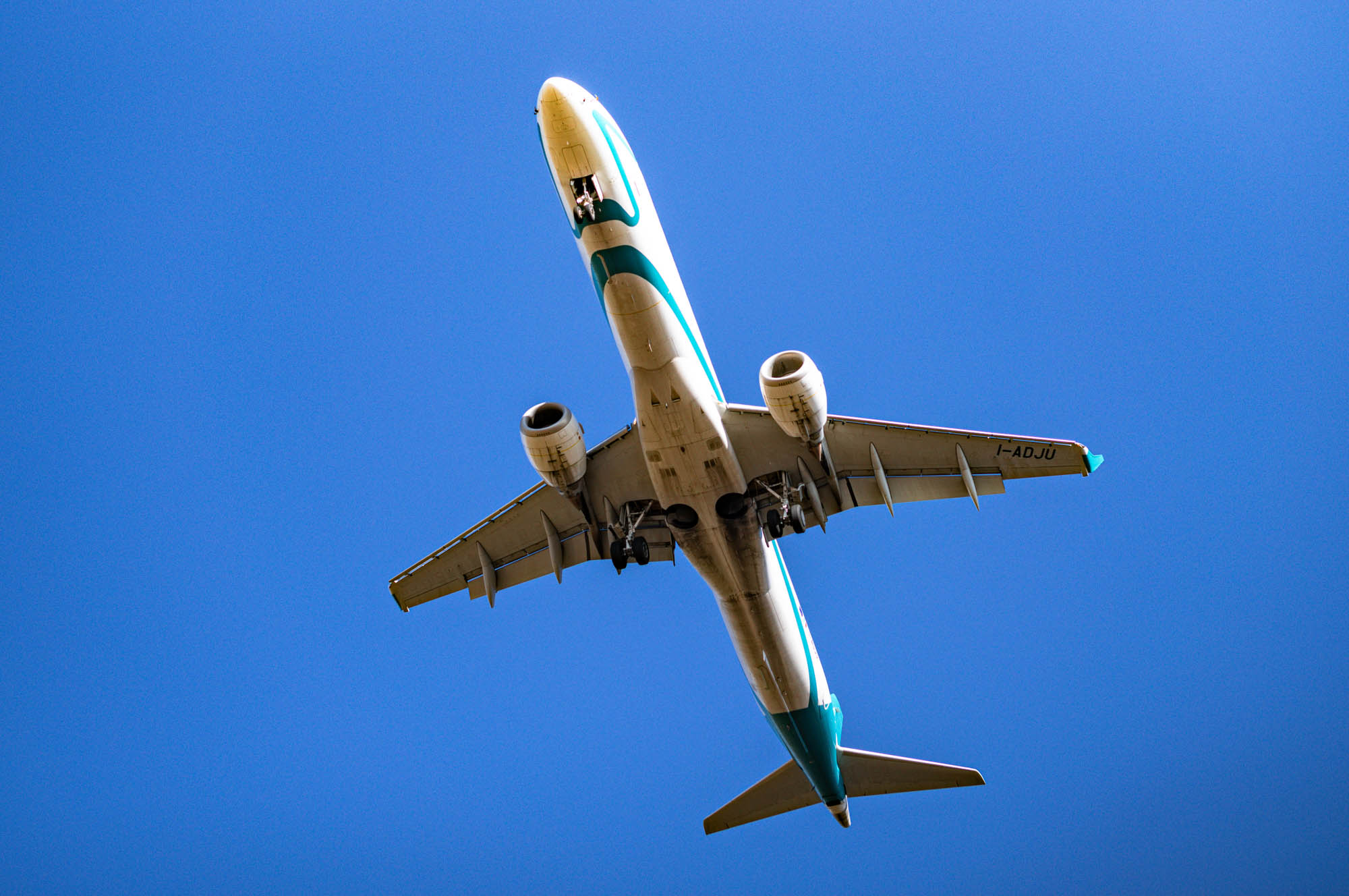 Airplane flying overhead against a clear blue sky, viewed from below, displaying wings and engines.