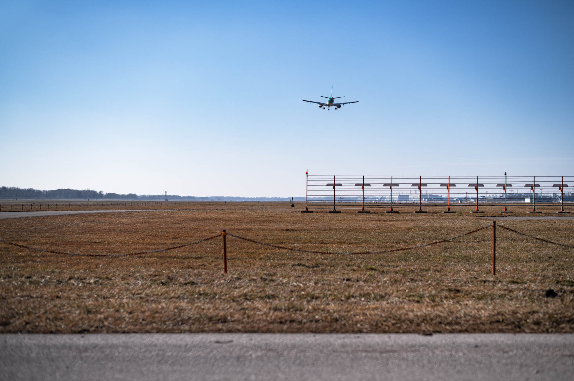 Airplane descending onto runway on clear day, with landing lights in foreground and blue sky backdrop.
