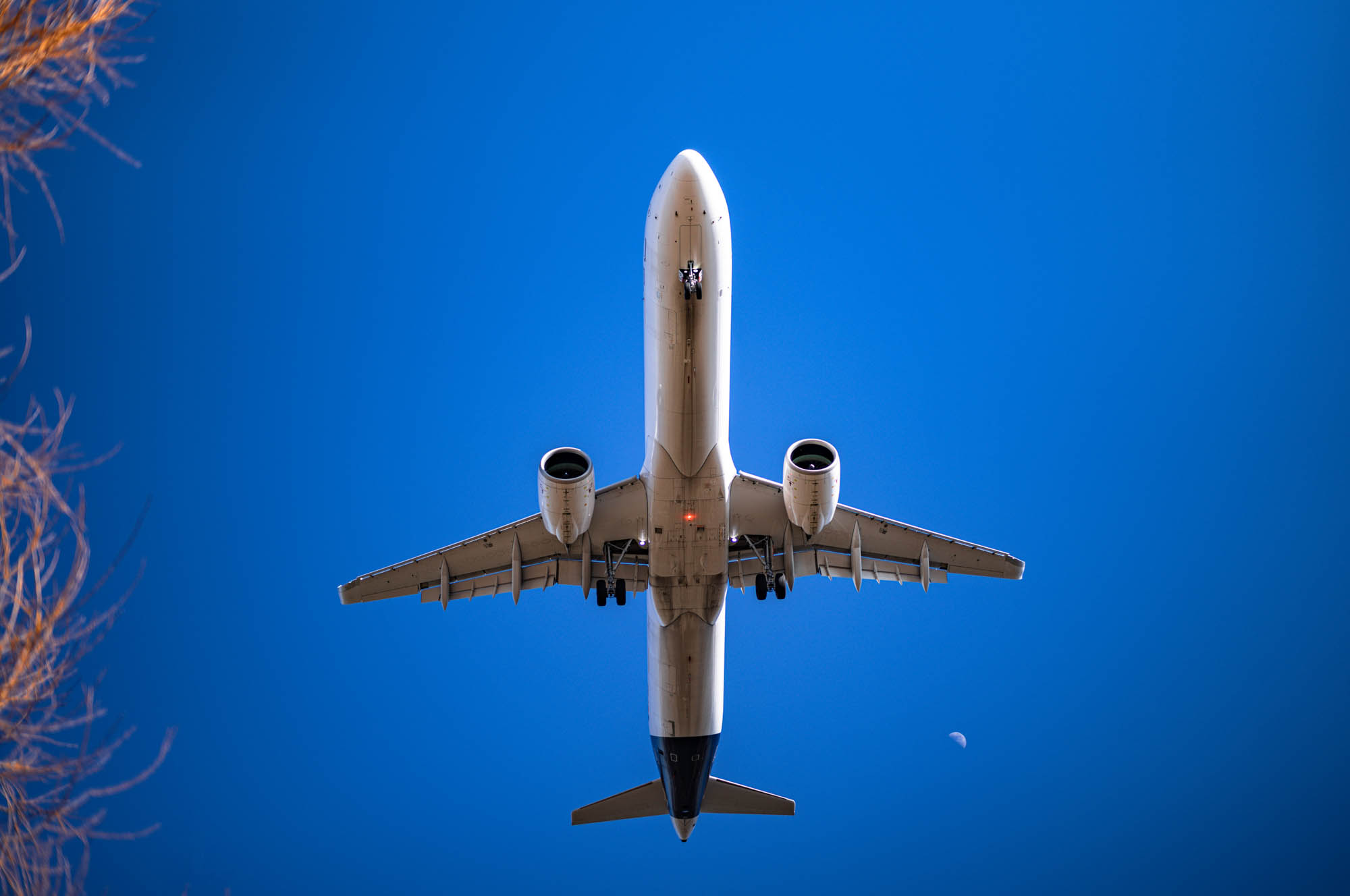 Airplane flying overhead against a clear blue sky with moon visible.