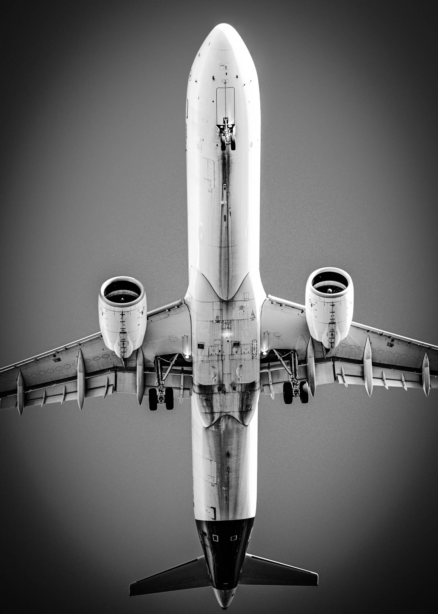 Black and white photo of an airplane flying overhead, showcasing its wings and engines against a clear sky.