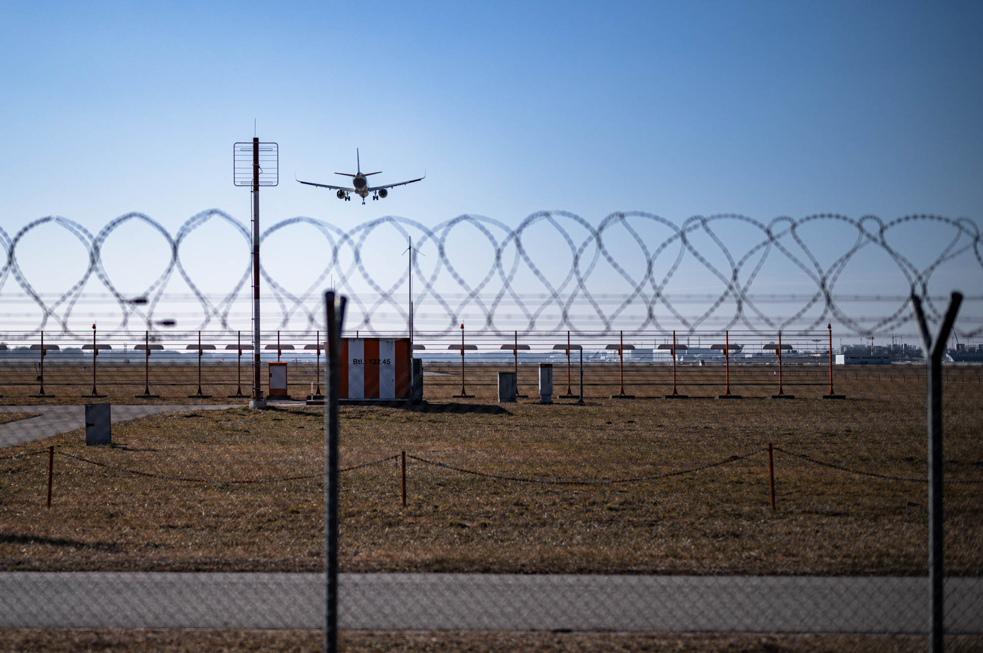 Airplane landing behind barbed wire fence at a sunny airport runway.
