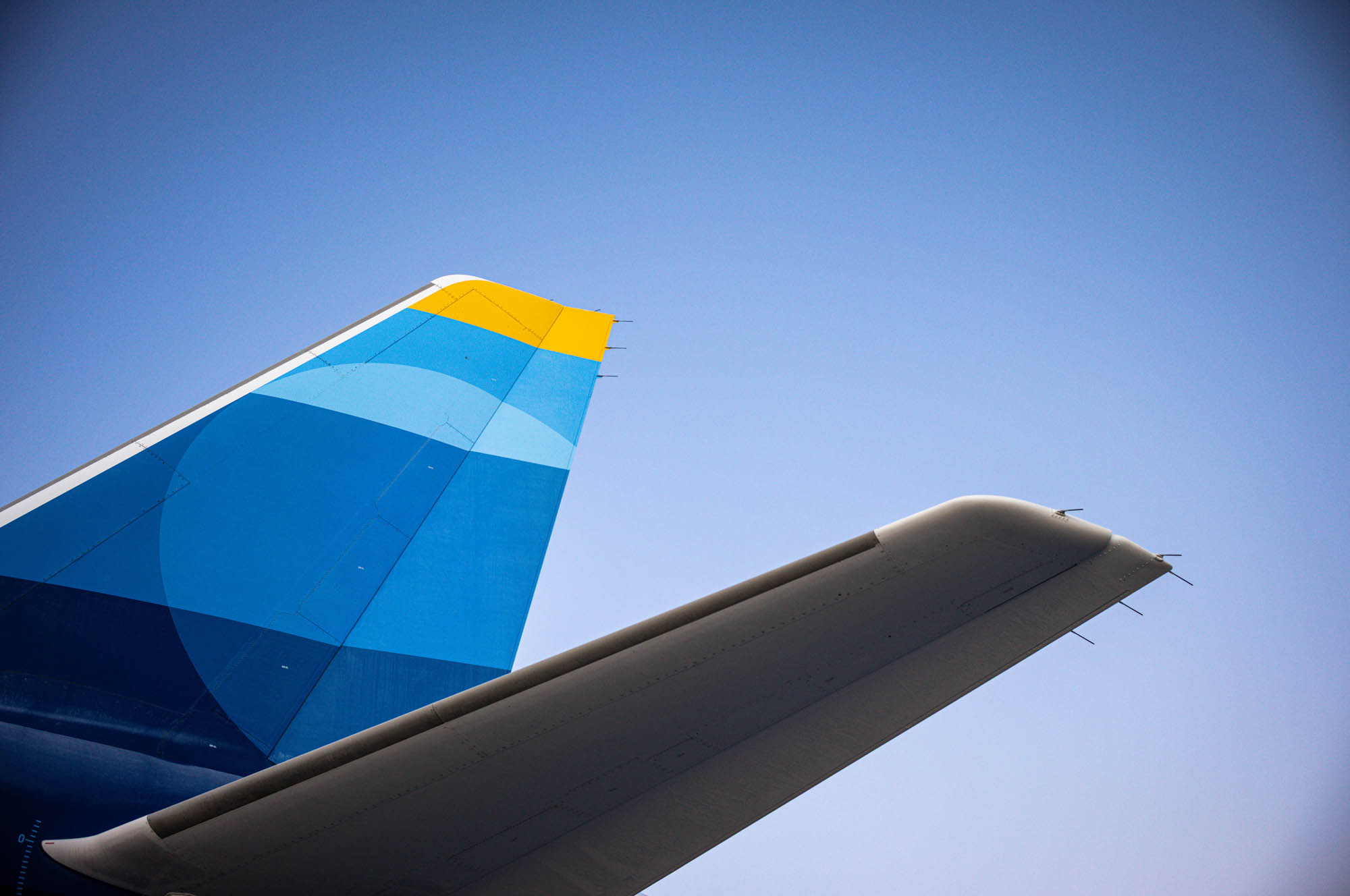 Colorful airplane tail against clear blue sky, featuring geometric design and bright colors, showcasing modern aviation style.