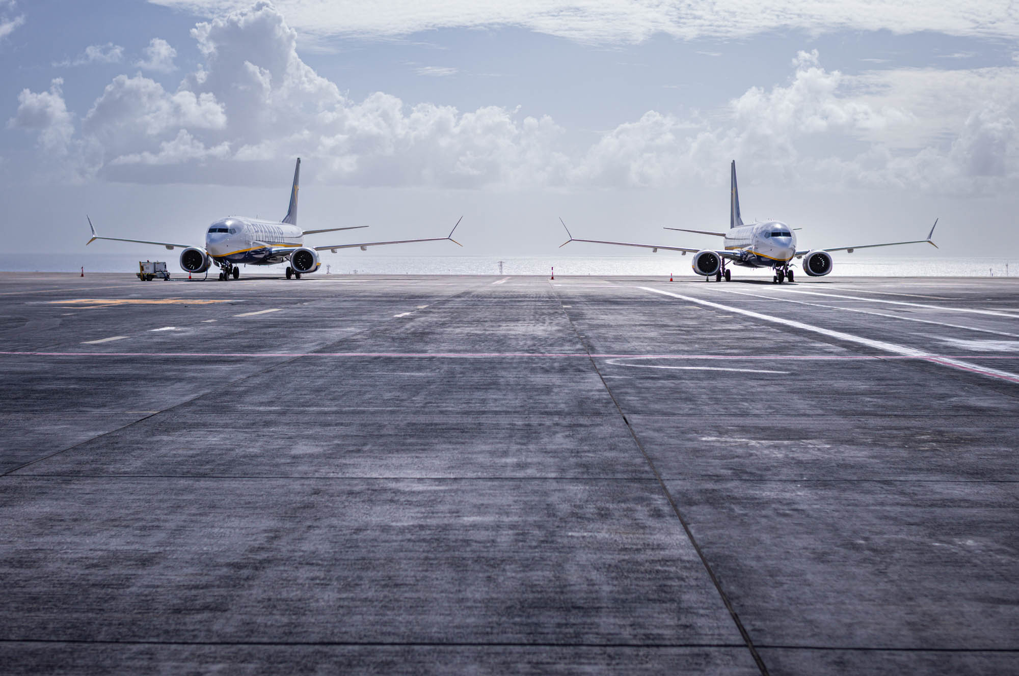 Two airplanes parked on an airport runway under a cloudy sky, ready for departure.
