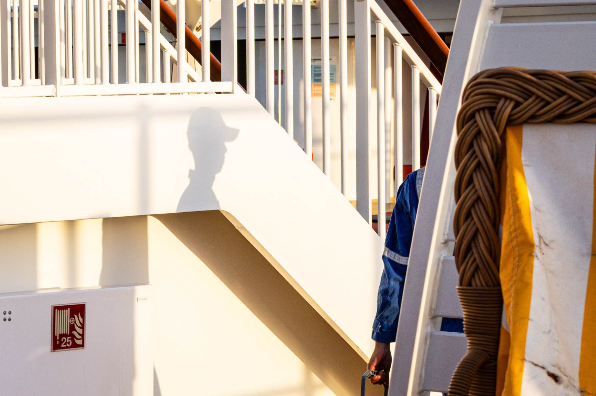 Shadow on a ship's stairs as a person in uniform walks by; nautical safety equipment visible.