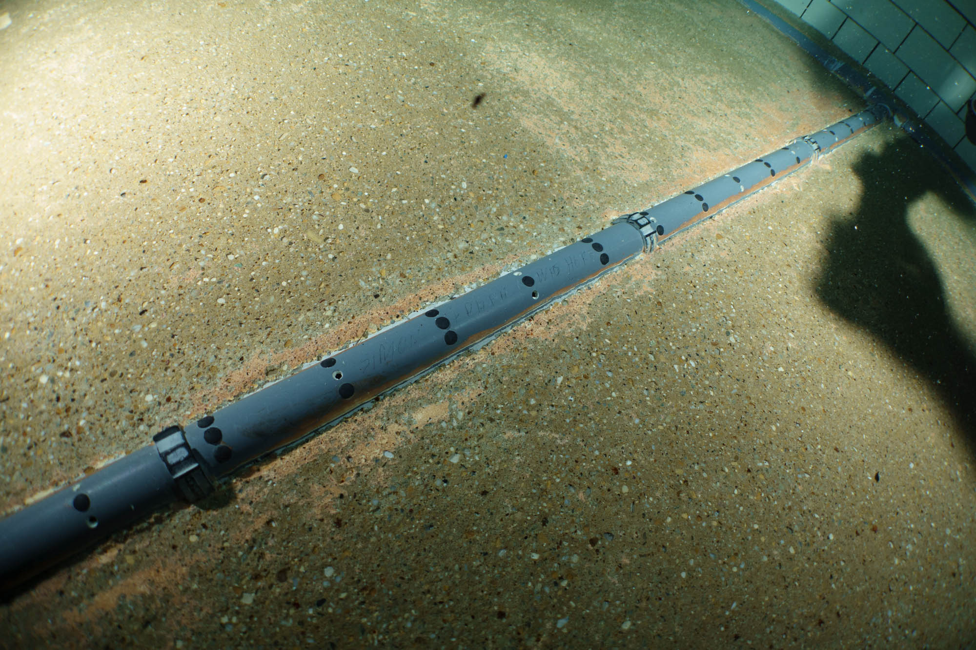 Underwater pool pipe system on tiled floor with visible shadow.