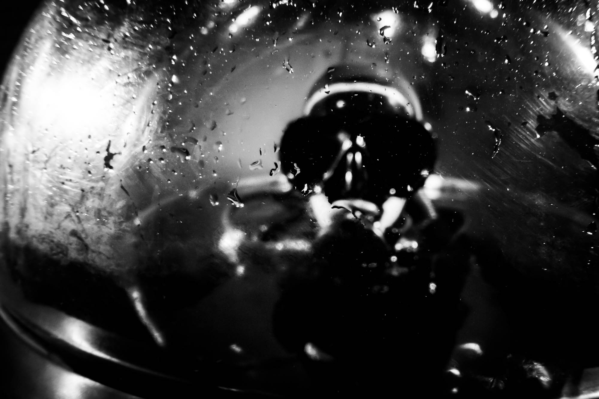 Black and white image of a person in a helmet, seen through droplets on a glass surface.