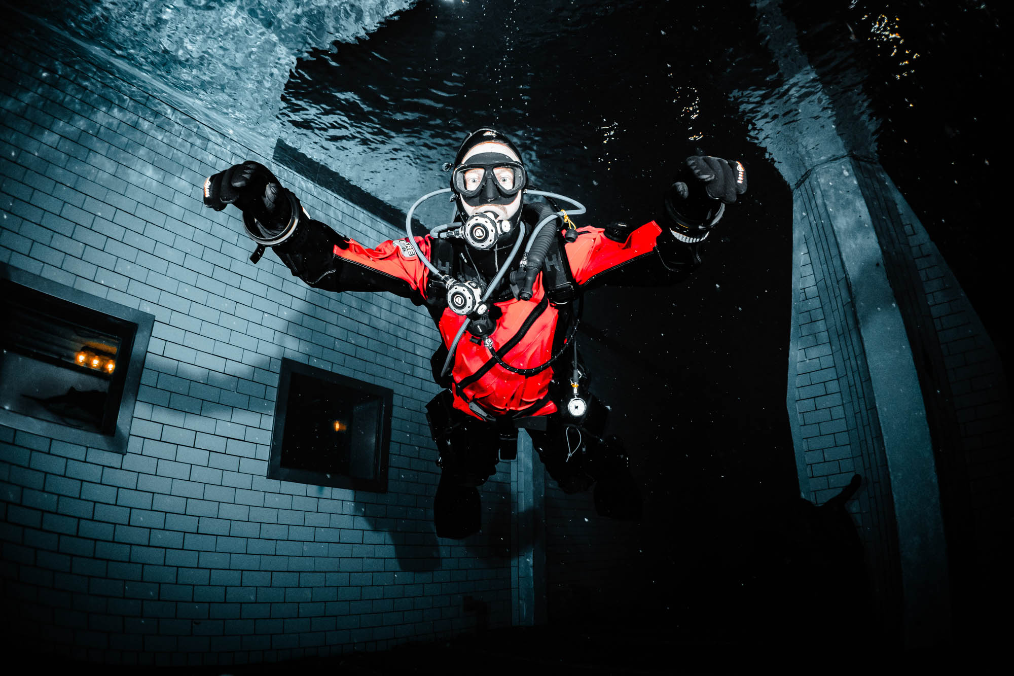 Diver in red suit underwater in dark pool, exploring with scuba gear.