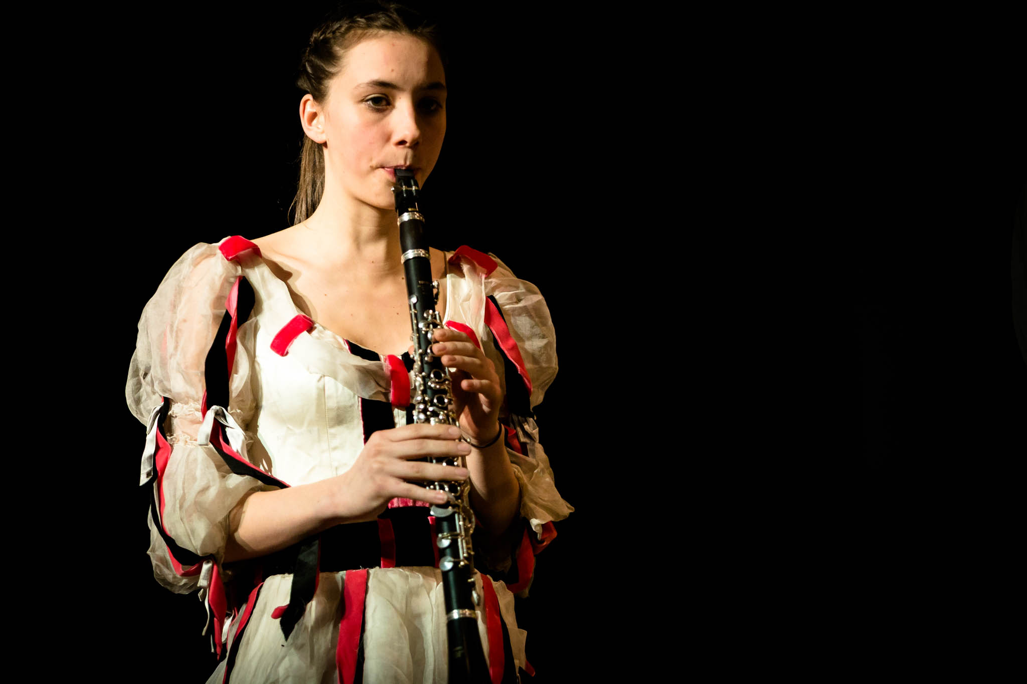 Woman in costume plays clarinet against a black background, emphasizing musical performance and artistic expression.