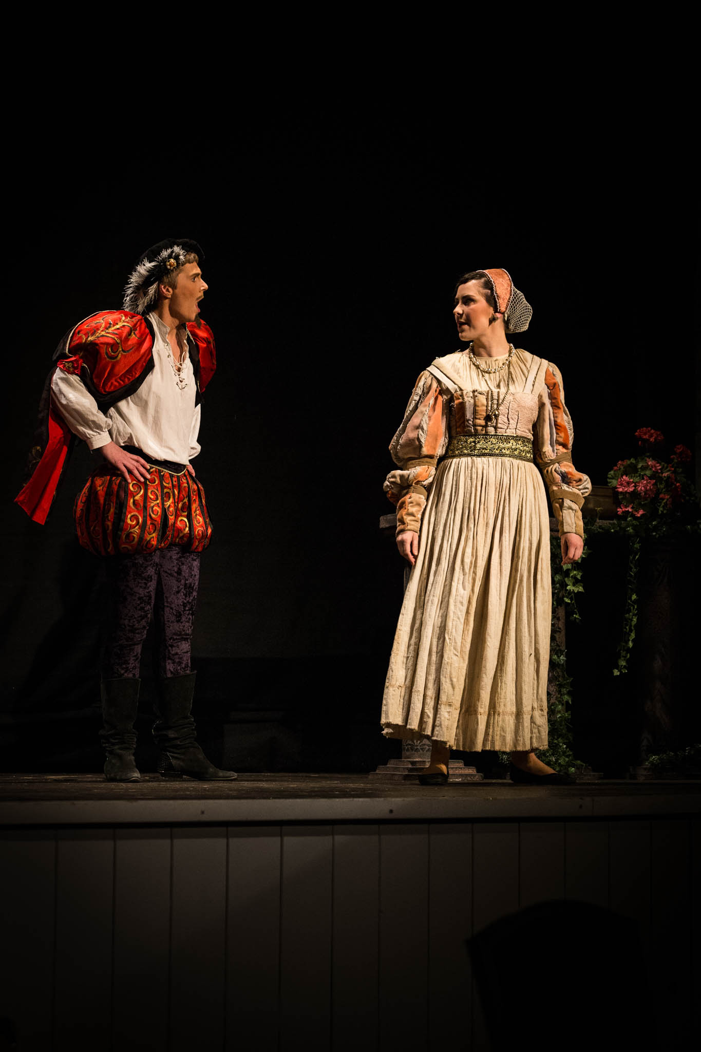 Two actors in Renaissance costumes engage in a theatrical performance on stage.