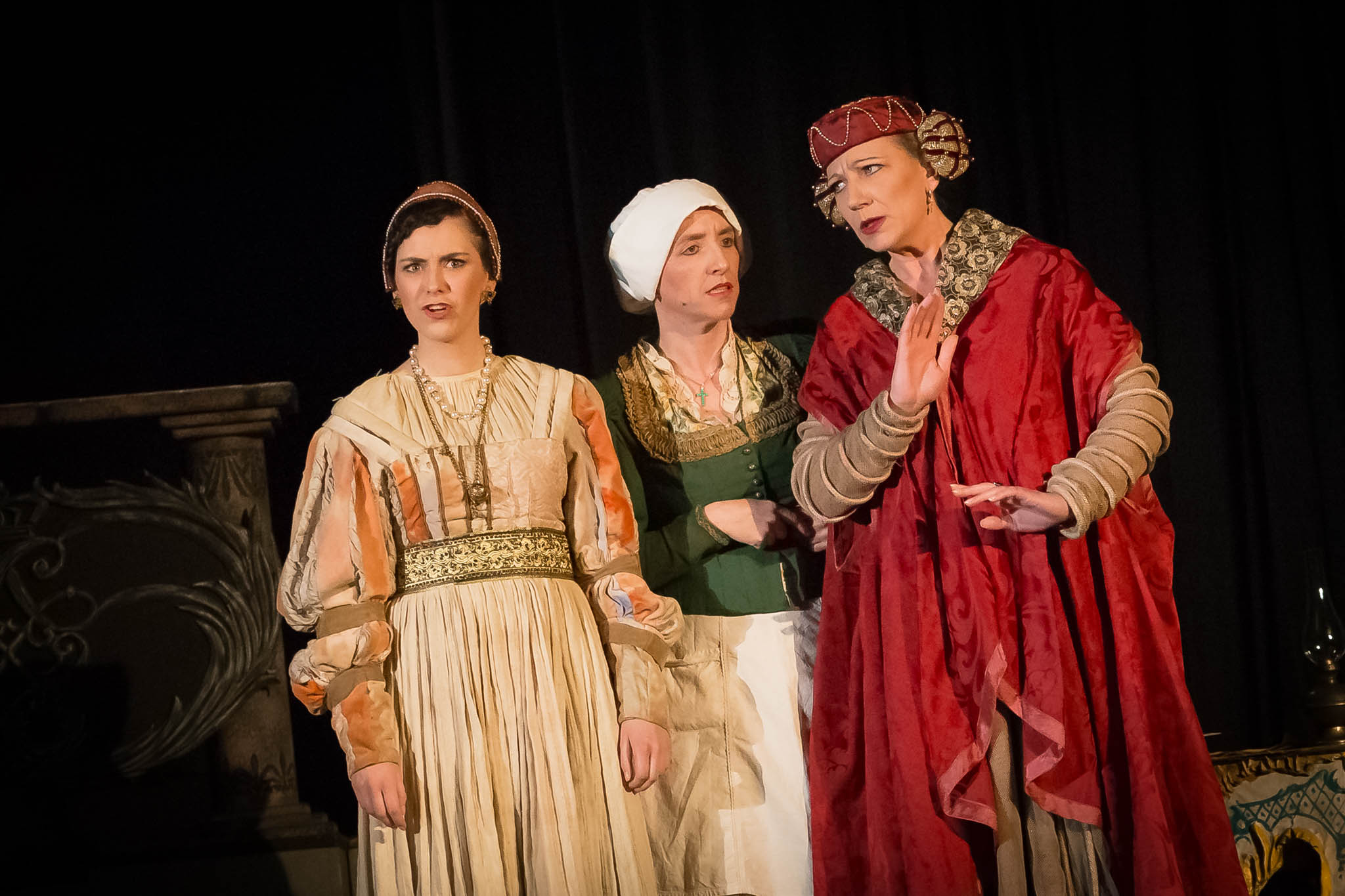 Three actors in Renaissance costumes perform a dramatic scene on stage.