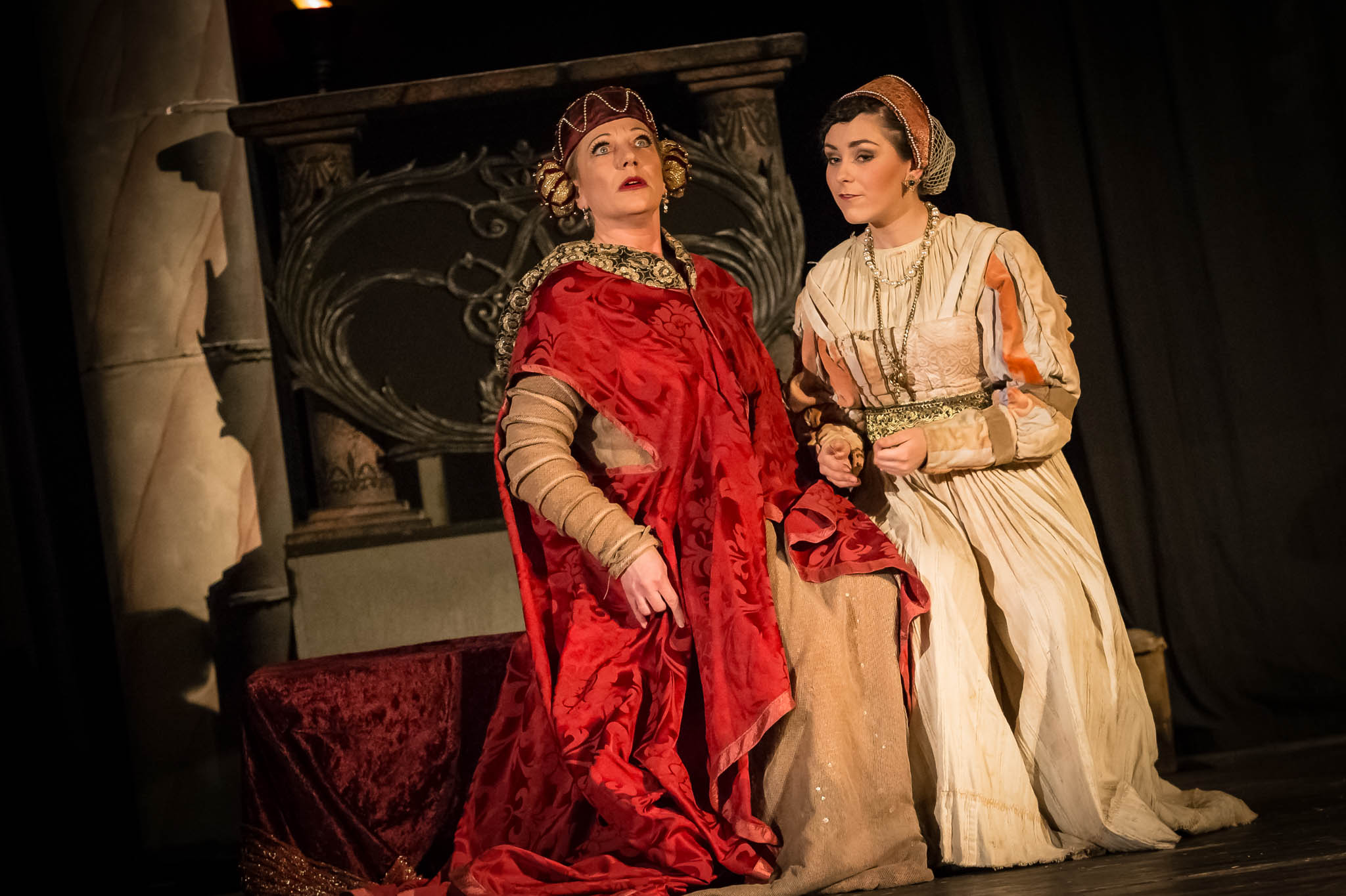 Two actors in elaborate medieval costumes performing on stage with dramatic expressions.