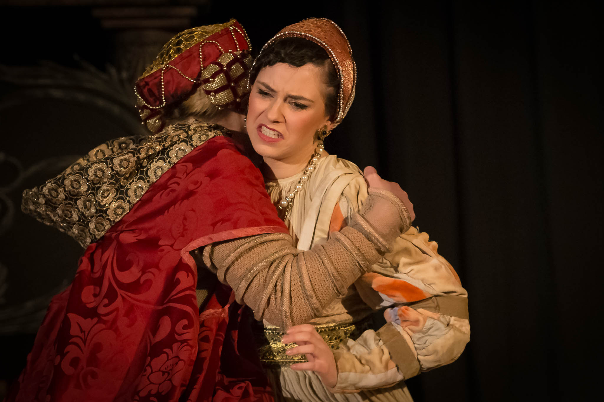 Actors in medieval costumes in a tense embrace on stage, dramatic expressions, dark backdrop.