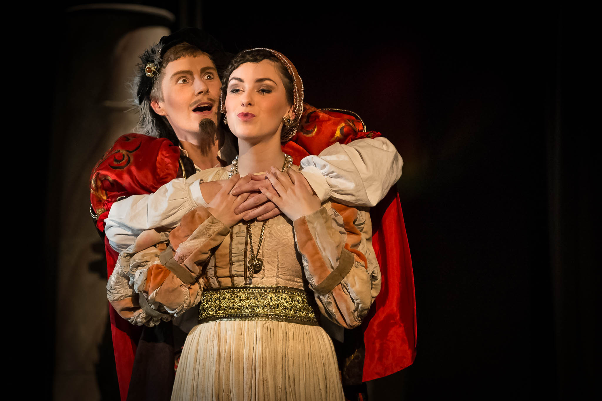 Two actors in period costumes perform passionately on stage, wearing ornate outfits with expressive gestures.