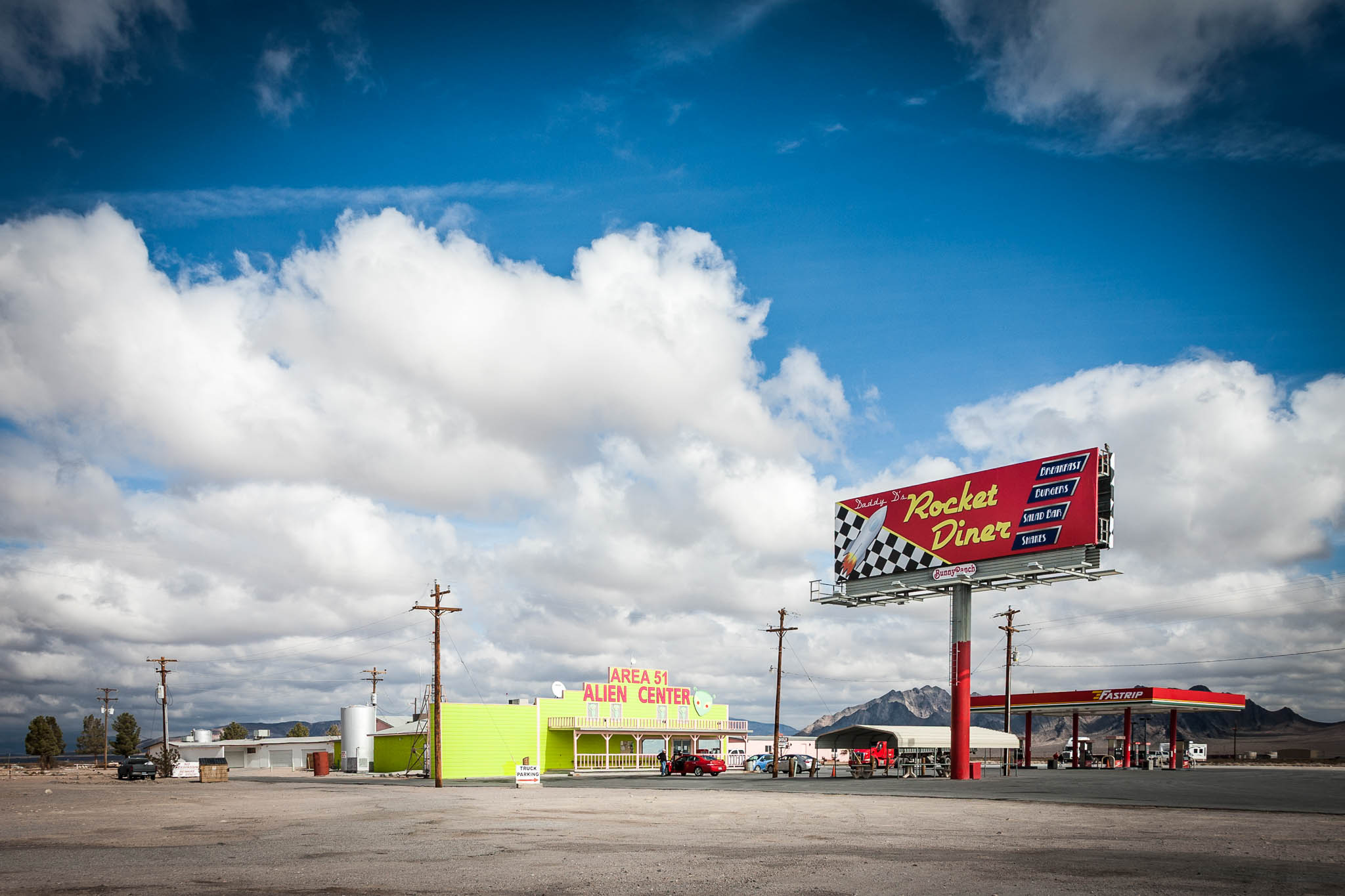 Retro roadside diner and Area 51 Alien Center under cloudy blue sky, Nevada desert landscape in background.