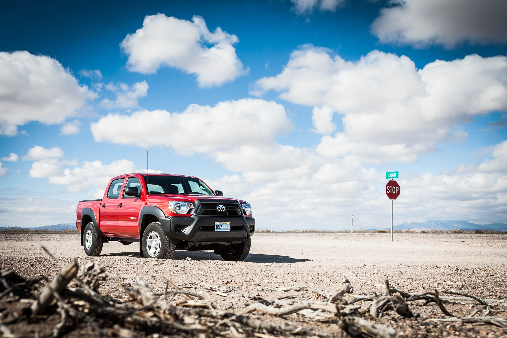 Red pickup truck on a dusty road under a cloudy blue sky with a stop sign nearby.