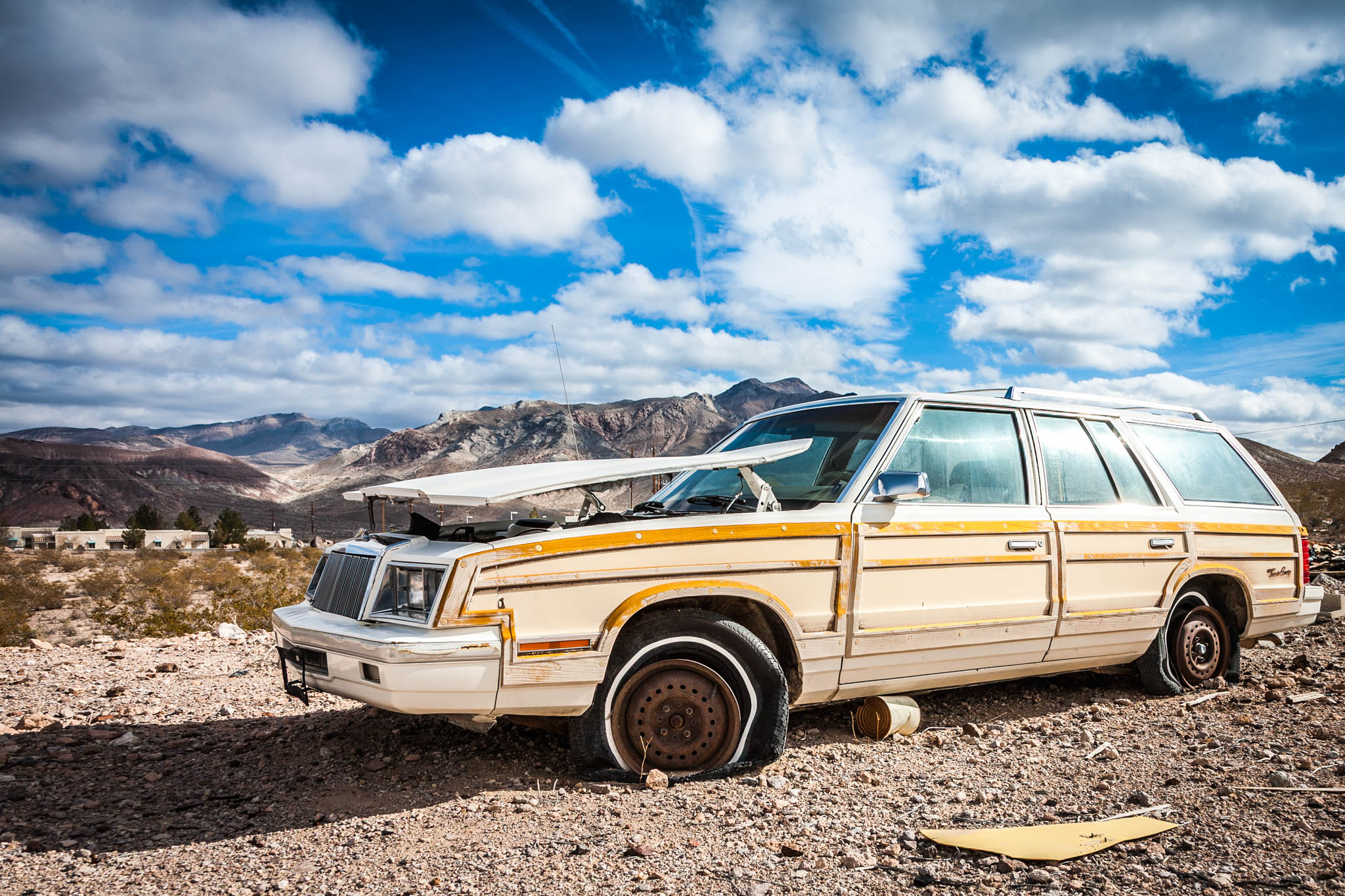 Abandoned, rusty station wagon with flat tires in a desert landscape under a bright blue sky.