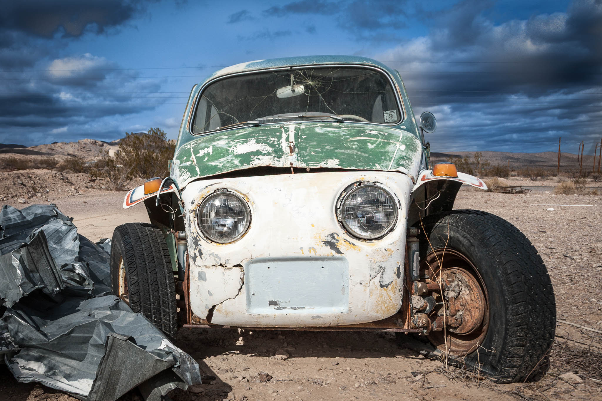 Front view of a rusty, vintage car with cracked glass, abandoned in a desert landscape under a cloudy sky.
