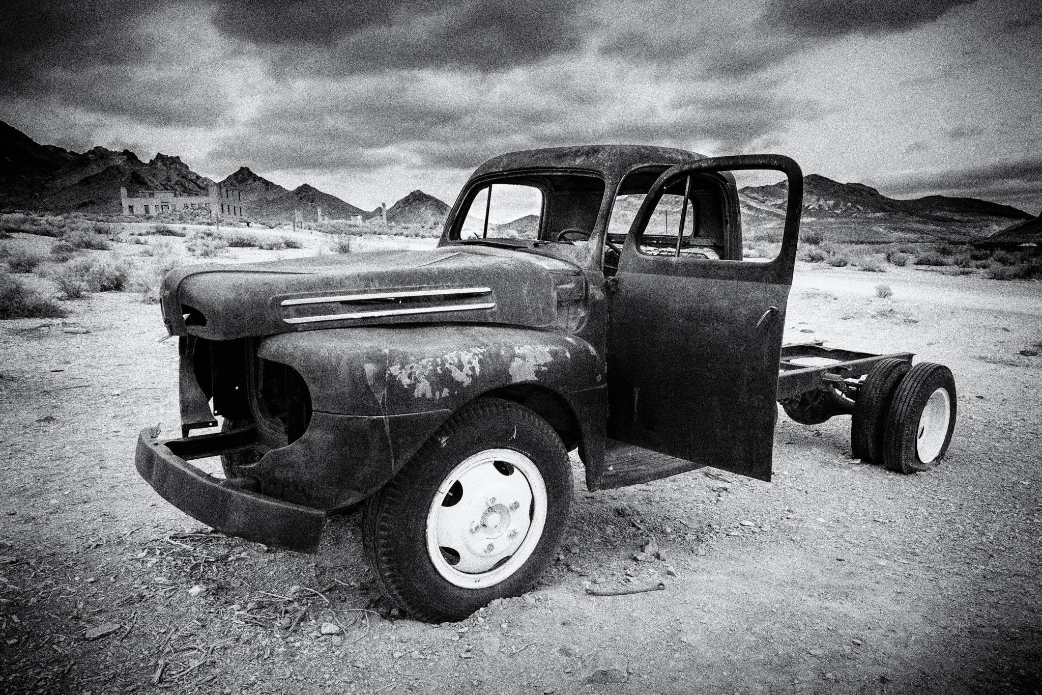 Rusty old truck in deserted landscape with mountains and cloudy sky in black and white.
