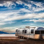 Exploring California & Death Valley – A Road Trip Through Ghost Towns, Highways & Desert Landscapes Shiny Airstream trailer parked in a vast desert landscape under a dramatic cloudy sky.