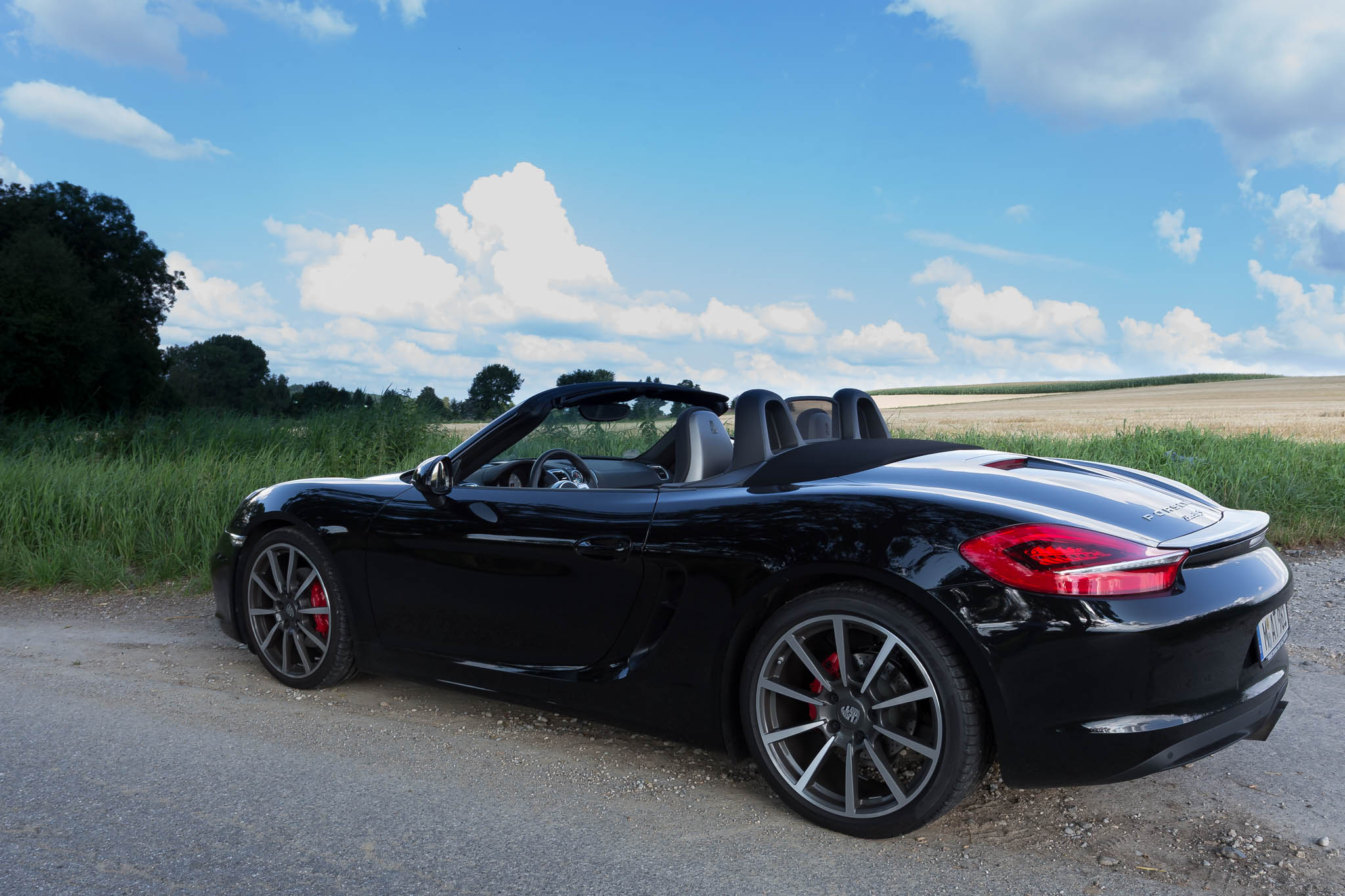 Black convertible sports car parked on a rural road under a bright blue sky with fluffy clouds.