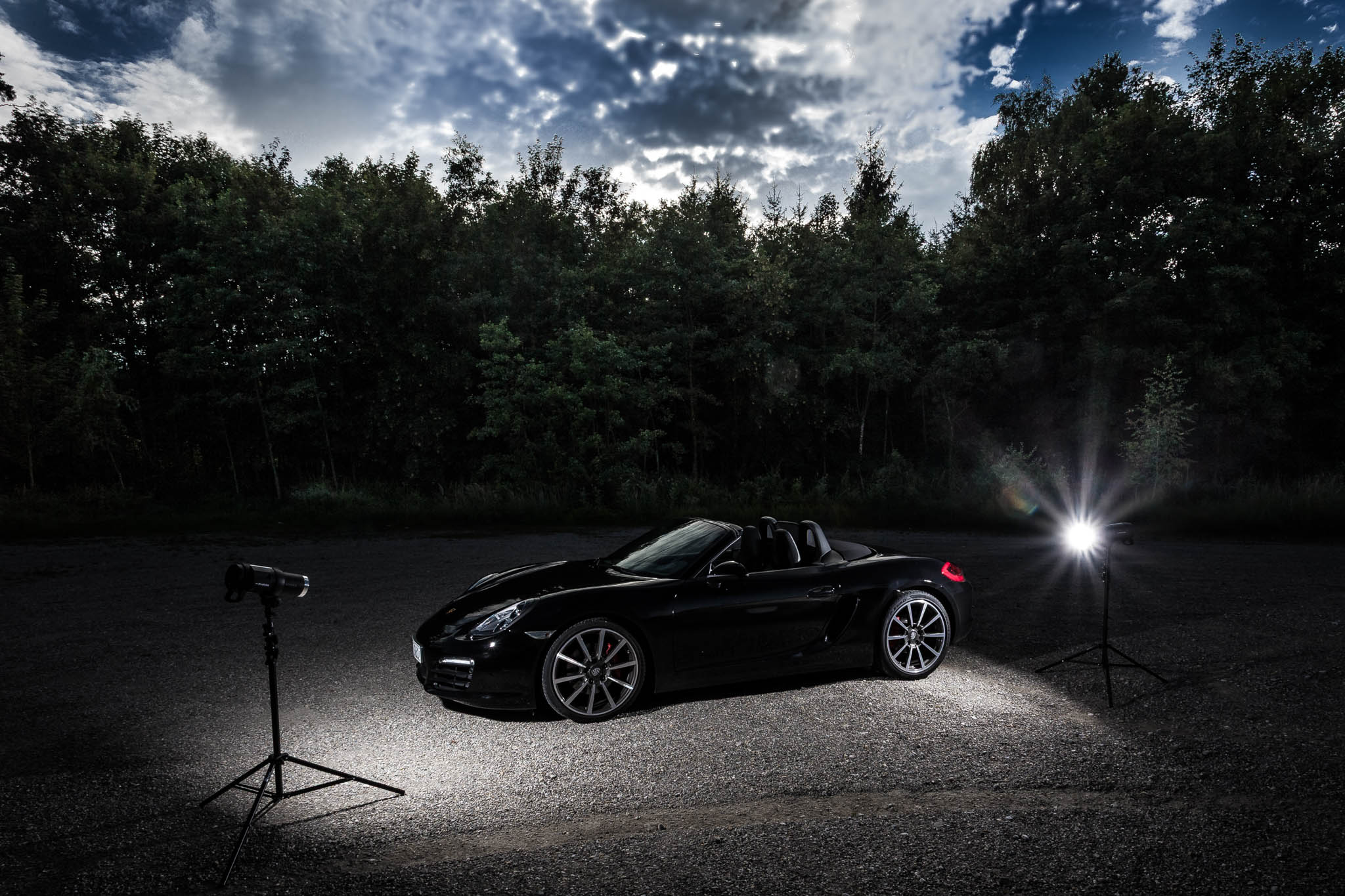 Convertible sports car under dramatic sky, illuminated by spotlights, with trees in the background.