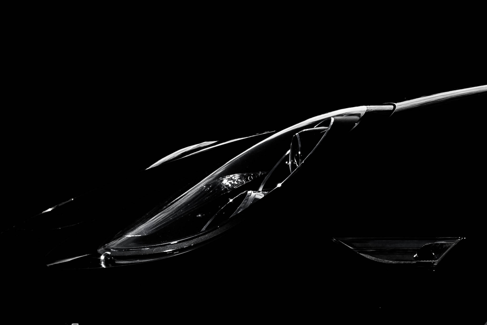 Close-up of a sleek car headlight against a black background, highlighting its modern design and glossy finish.