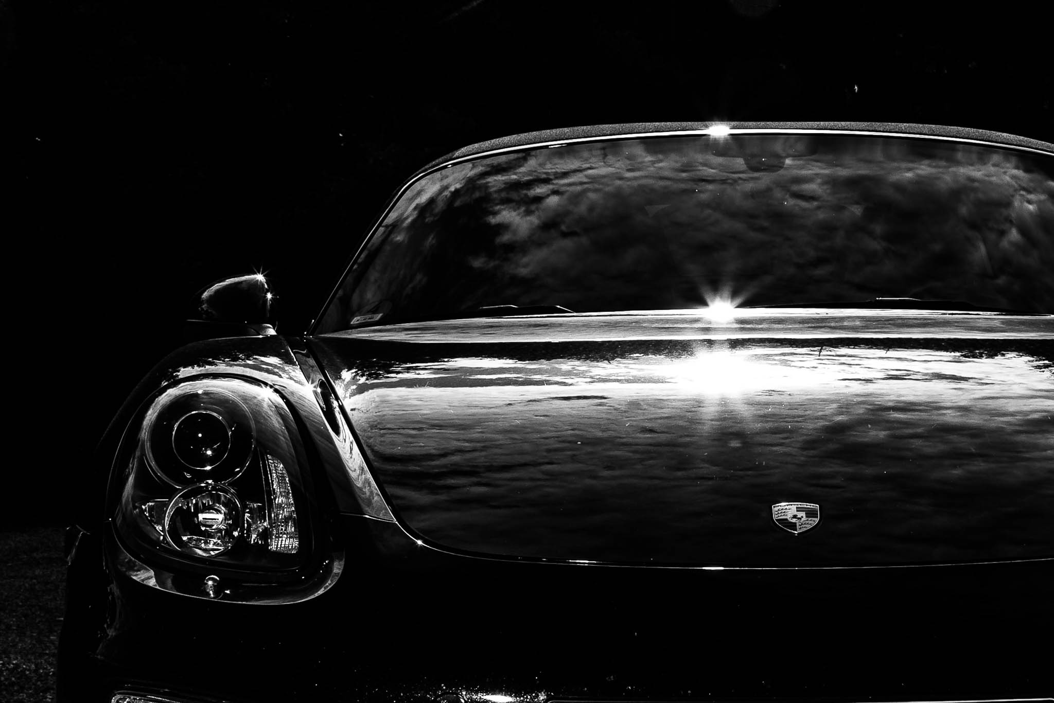 Sleek black luxury car front with shiny reflections and striking headlamp against a dark background.