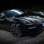 Sleek black convertible sports car parked on gravel with a reflective hood and stylish alloy wheels.