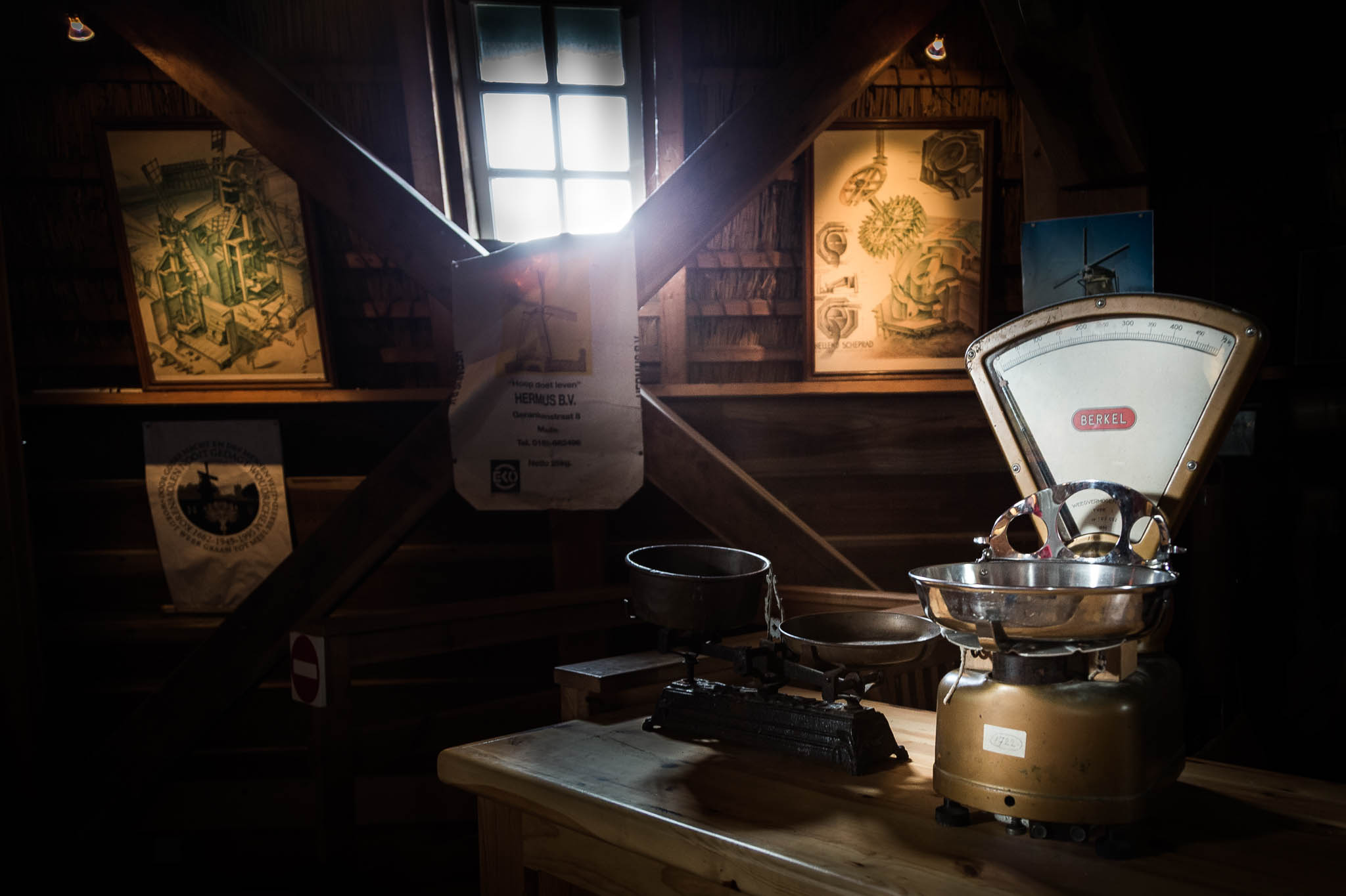 Vintage scales on wooden table in dimly lit room with antique posters and window in background.