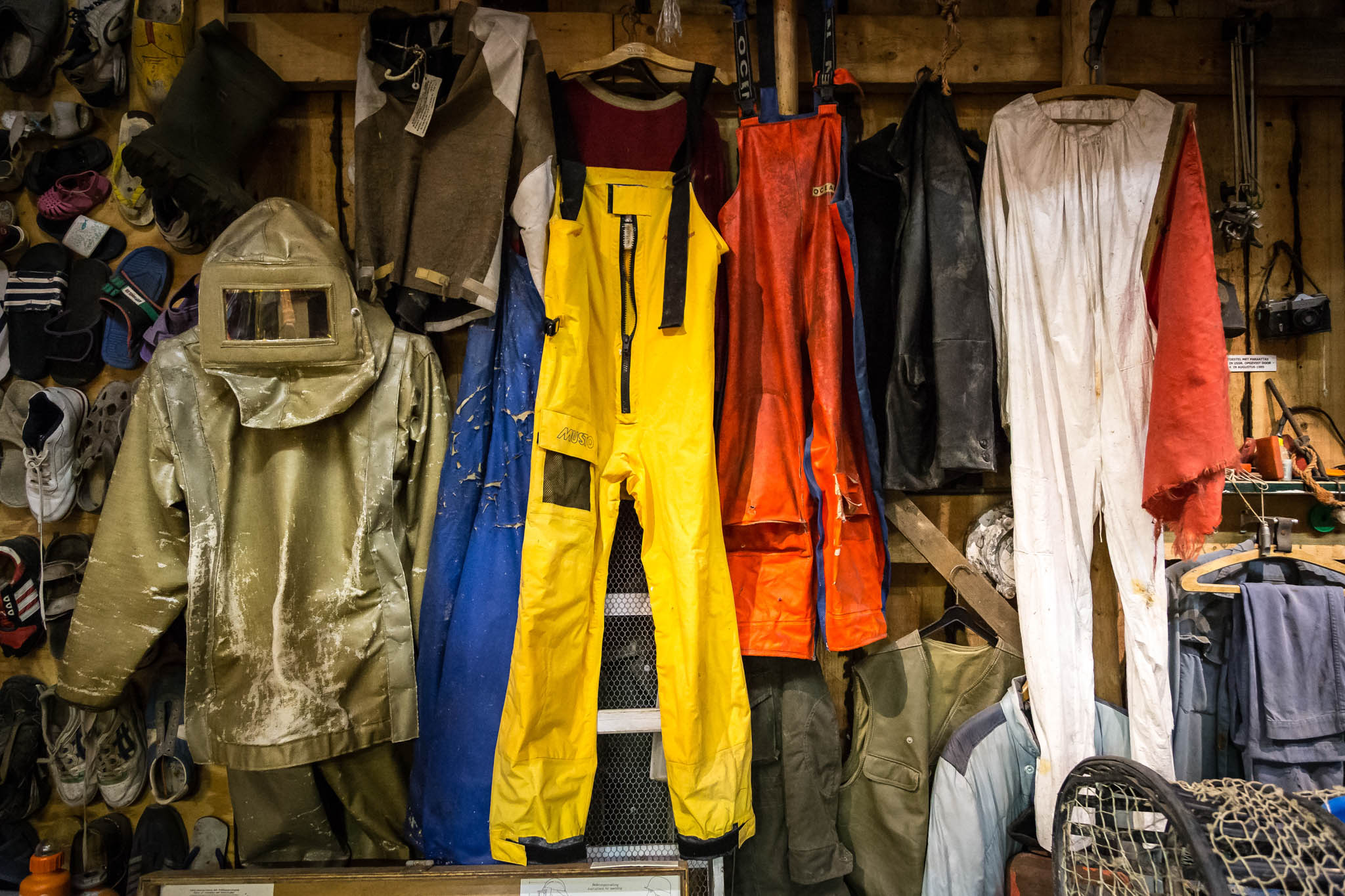 Colorful protective workwear and boots hanging on a wooden wall in a workshop setting.